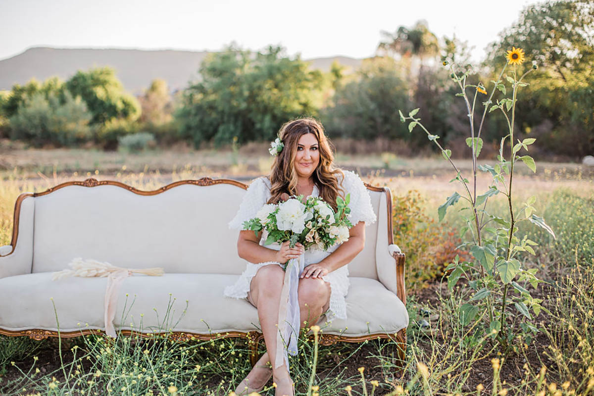 Woman in white dress with flowers on vintage sofa outdoors