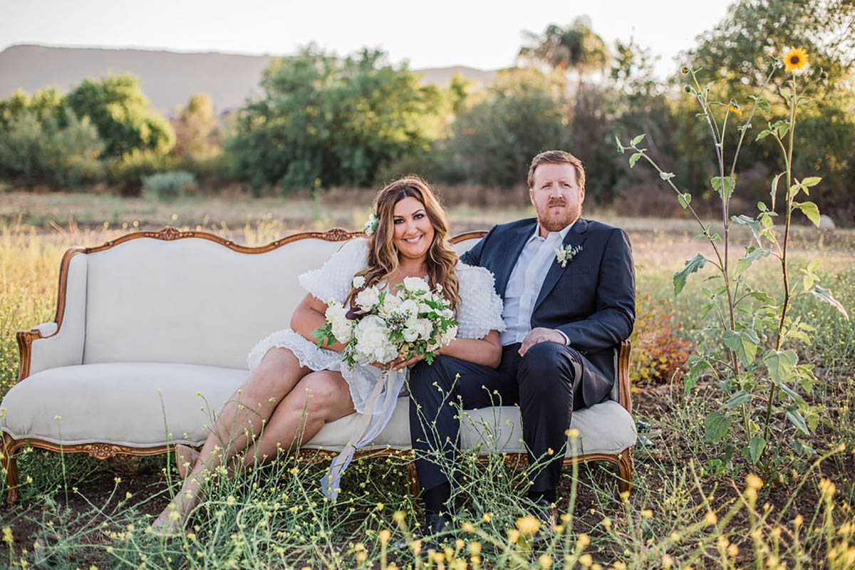 Bride and groom sit on a sofa in a field wedding photo