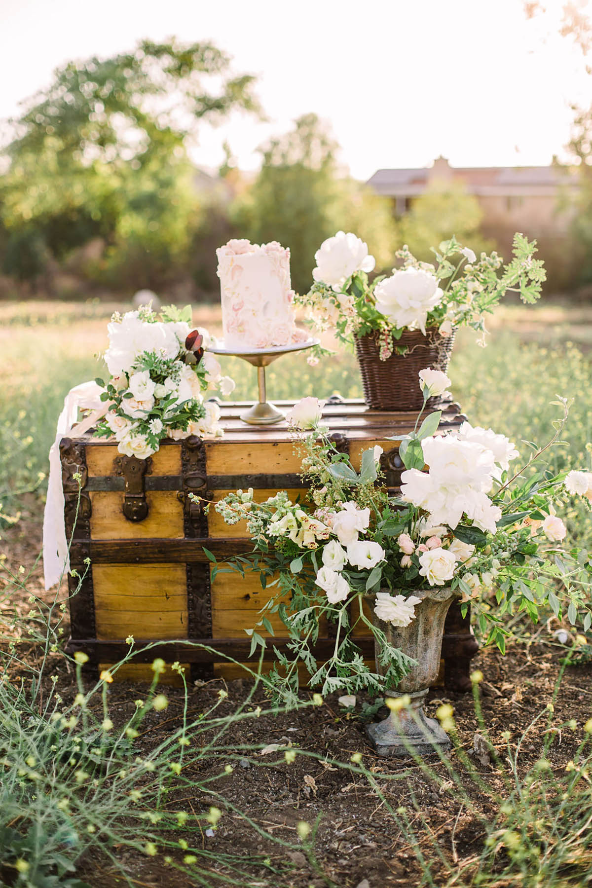 Rustic wedding cake and flowers on antique trunk outdoors
