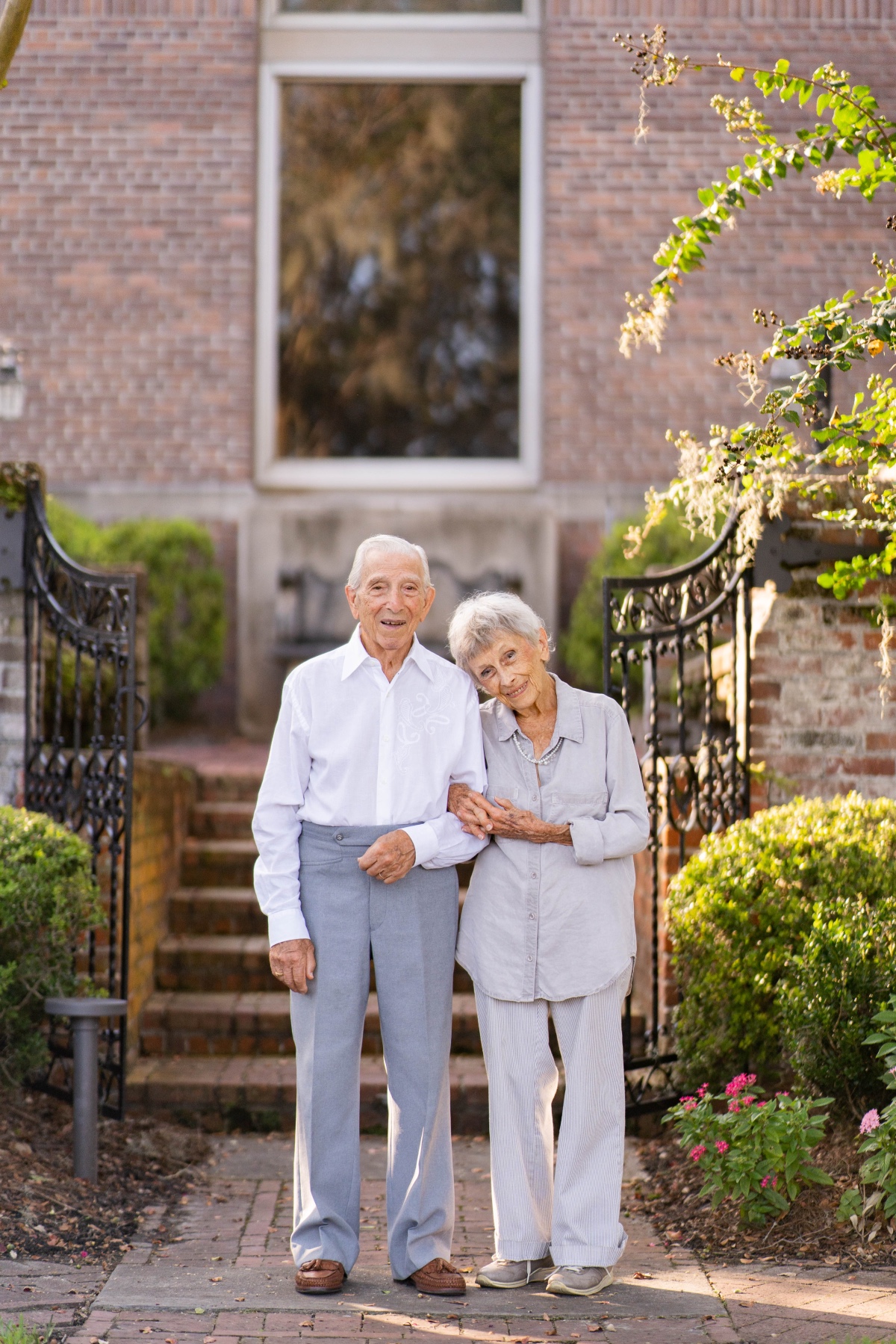 Senior couple holding hands in front of a brick house