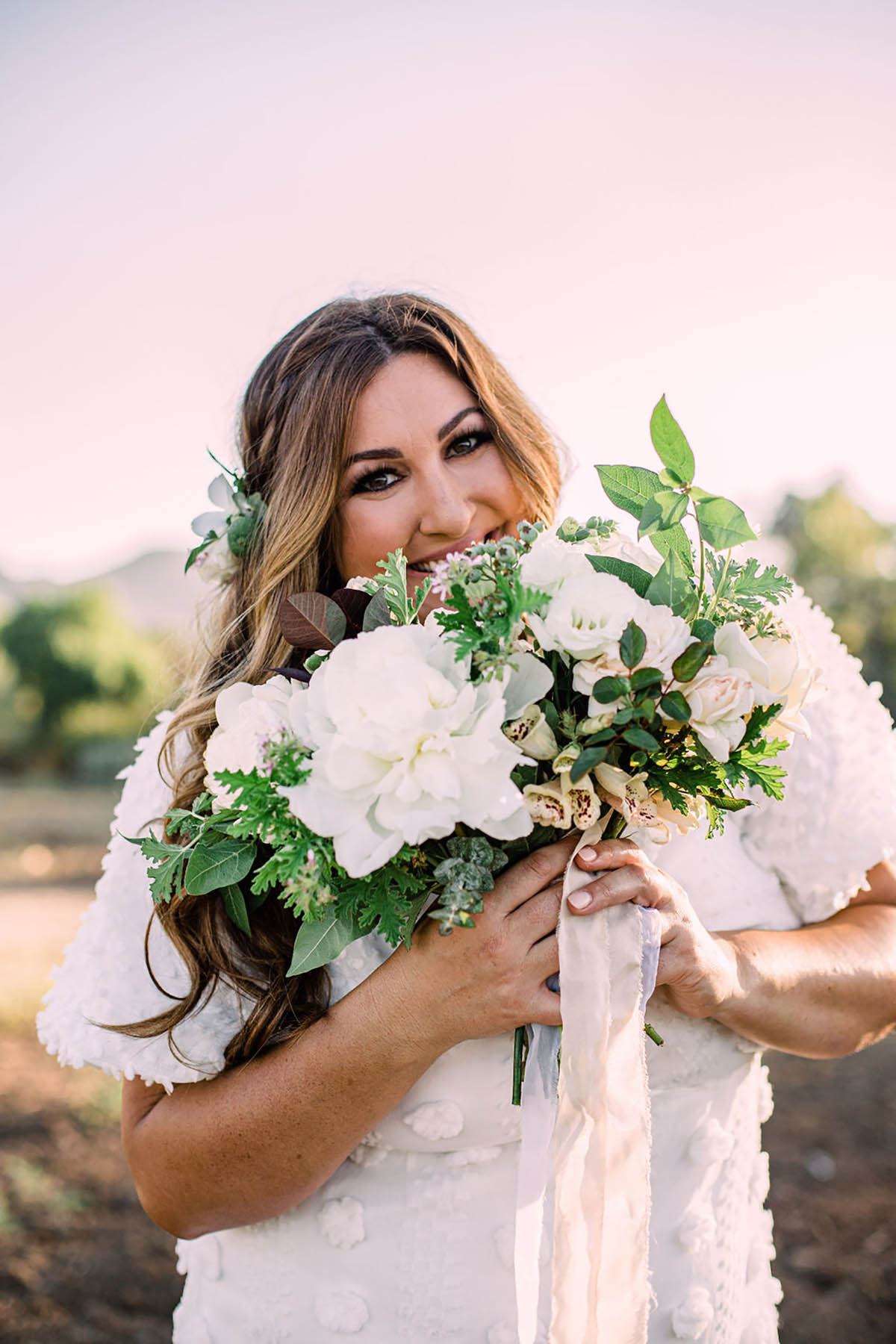 Bride smiling holding white flower bouquet outdoors
