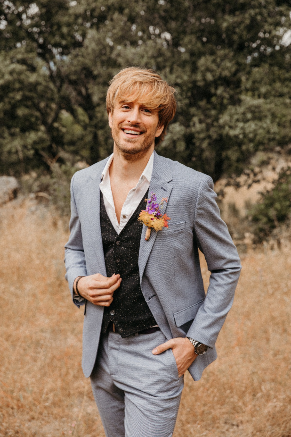 Smiling groom in light grey suit, vest, and floral boutonniere