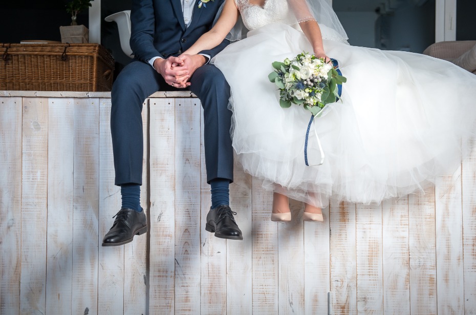 Newlywed couple sitting, holding hands, bride with bouquet
