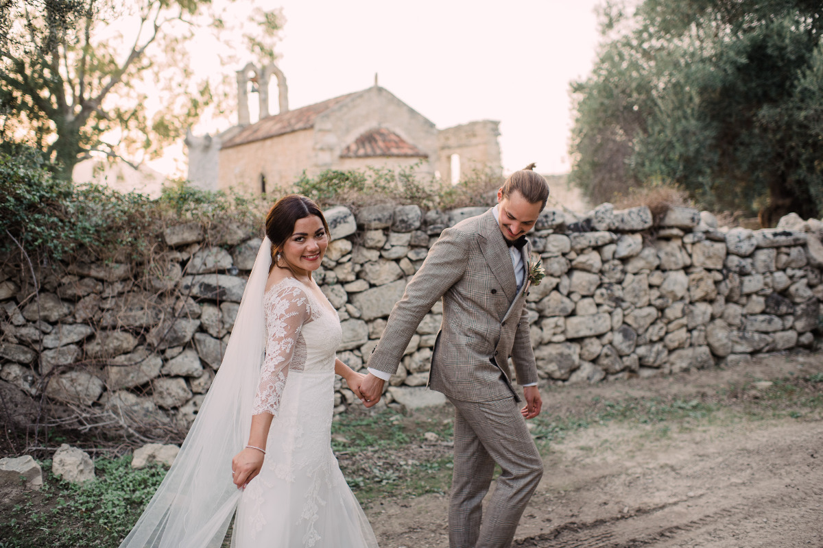 Happy bride and groom holding hands near rustic chapel