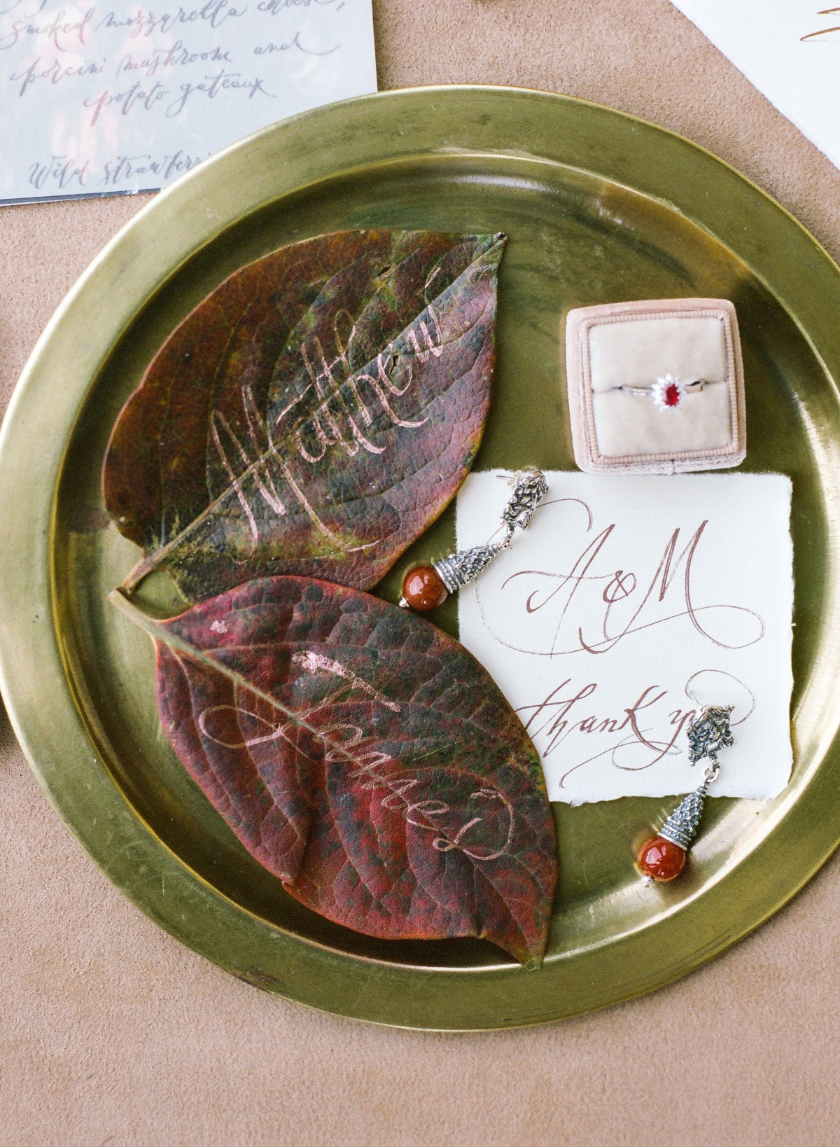 Wedding details with leaf name cards and jewelry on a brass tray