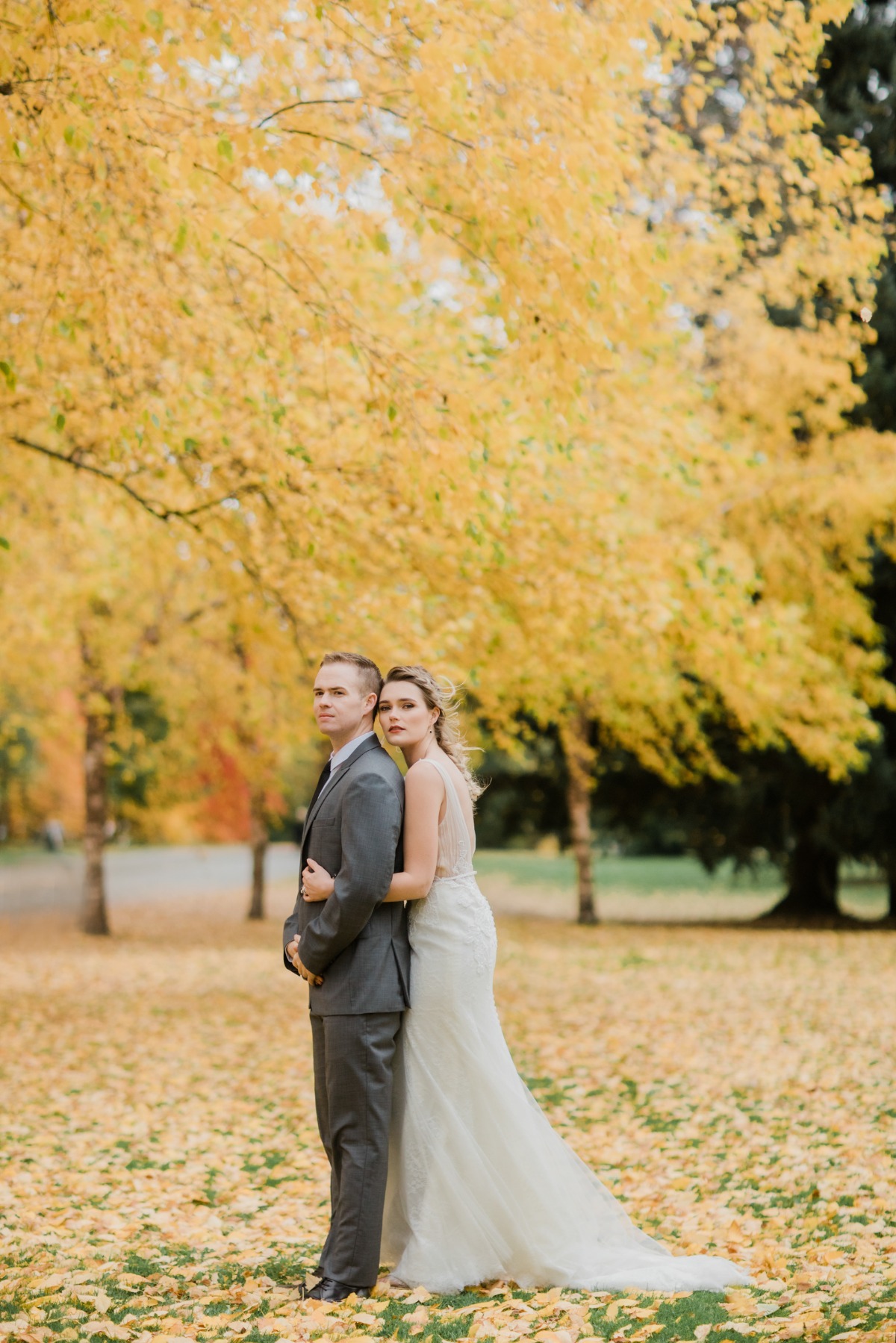 Bride and groom embrace in a park with yellow foliage during autumn
