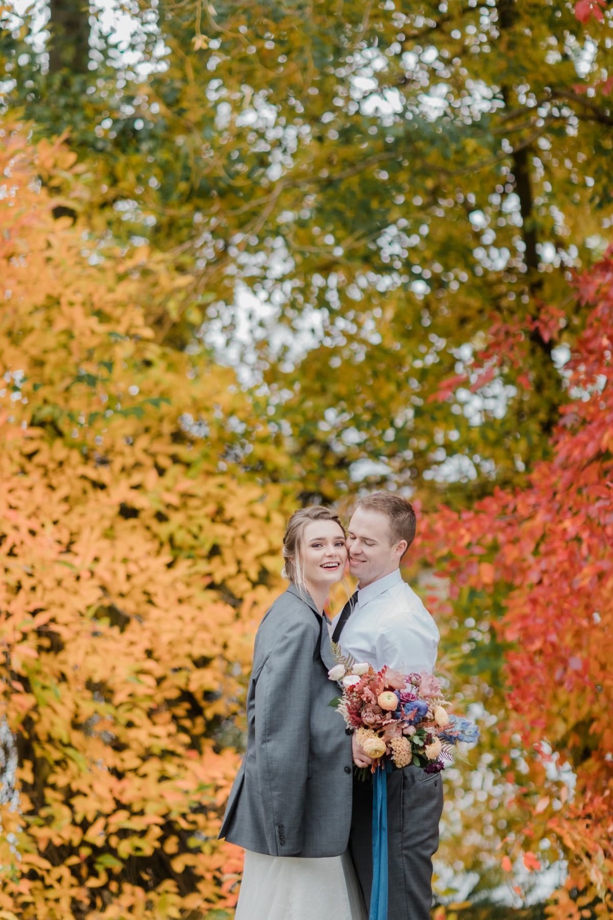 Newlyweds embrace with fall foliage in the background, joyful moment