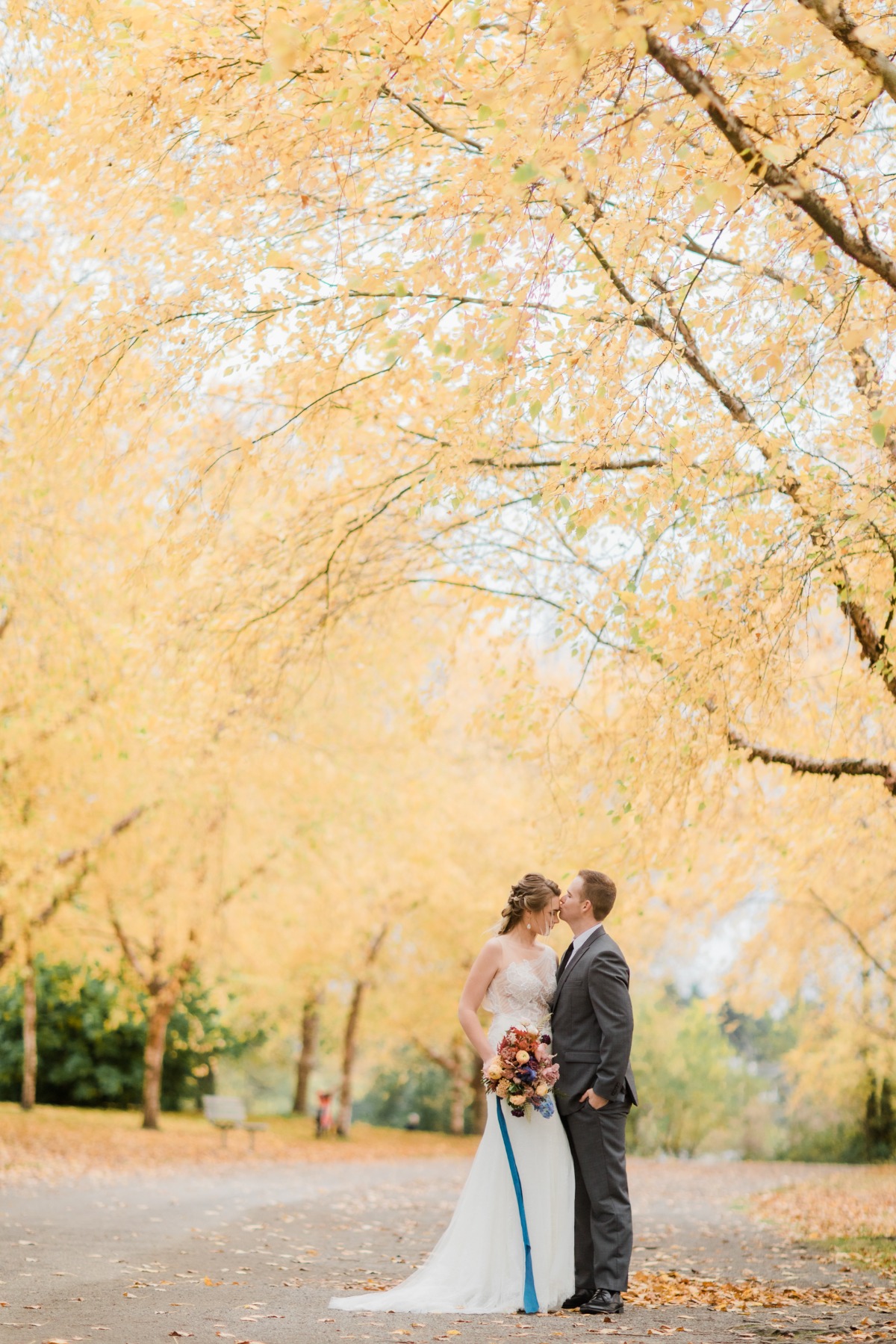 Bride and groom kiss under autumn trees on wedding day