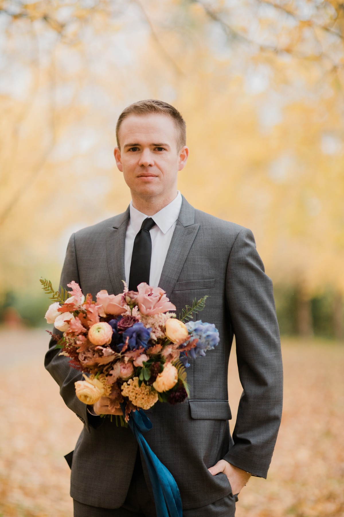 Groom in gray suit holds bouquet of flowers for autumn wedding