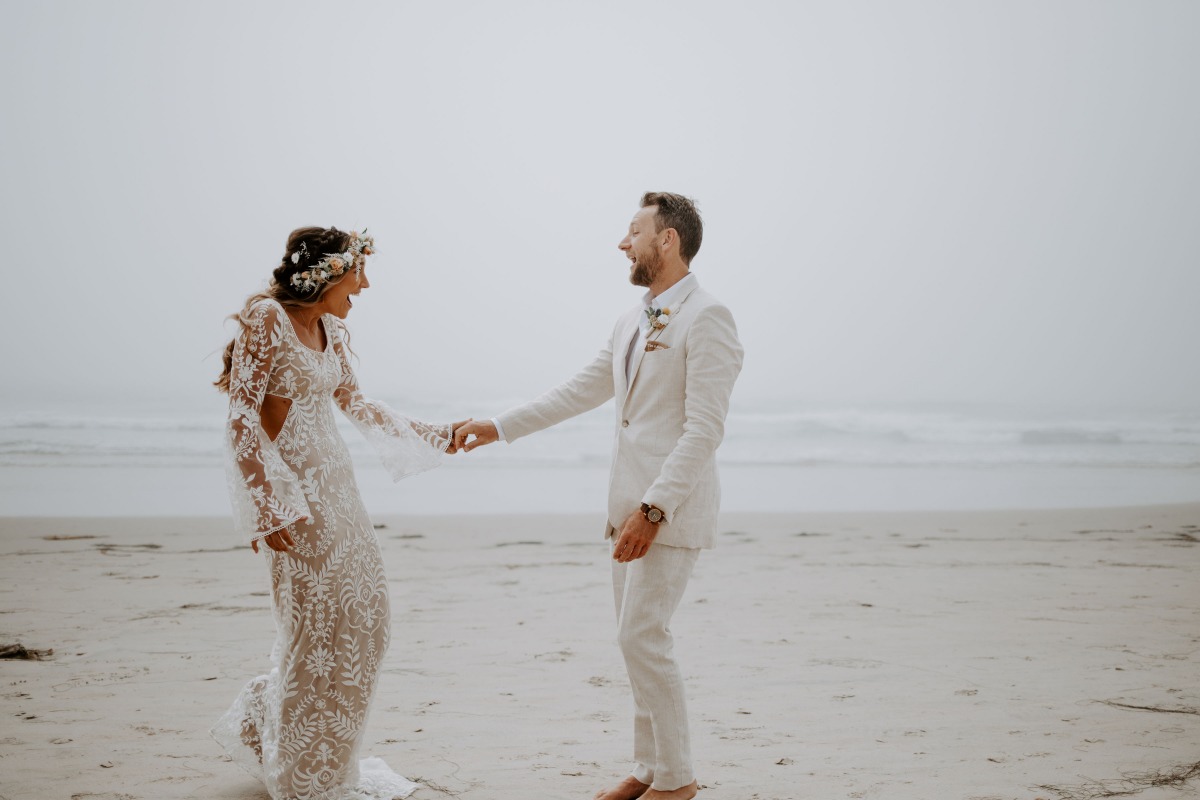 Newlyweds laugh as they hold hands on the beach, happy and in love