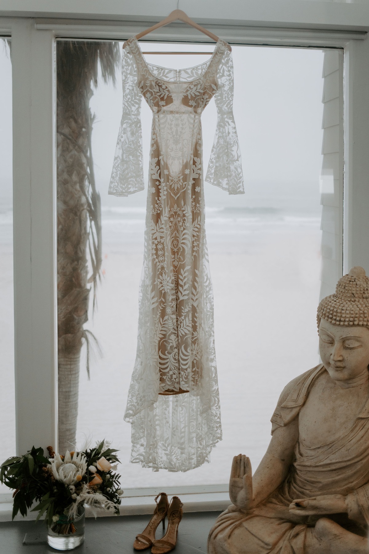 Lace wedding dress hanging near beach and Buddha statue
