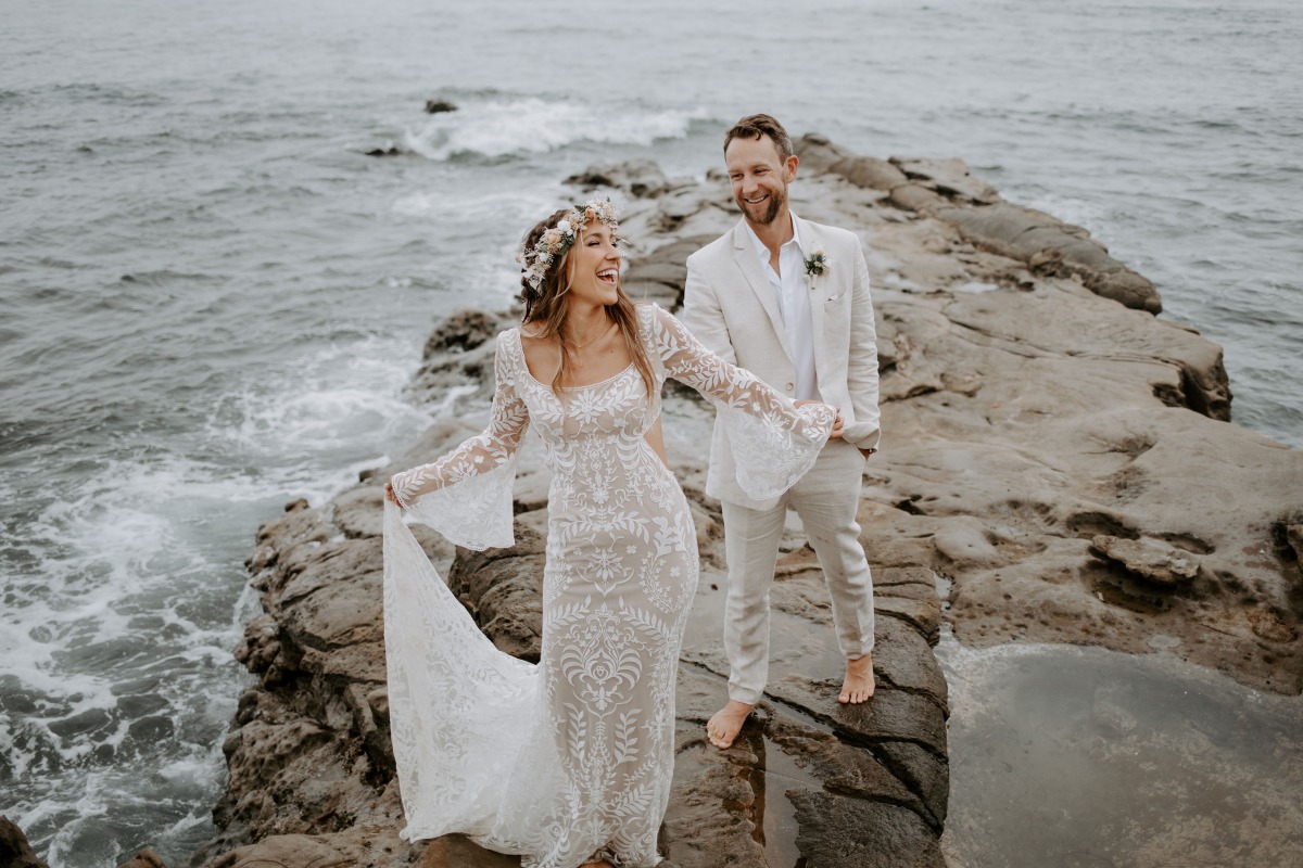Bride and groom laughing happily on the rocky shore at their wedding