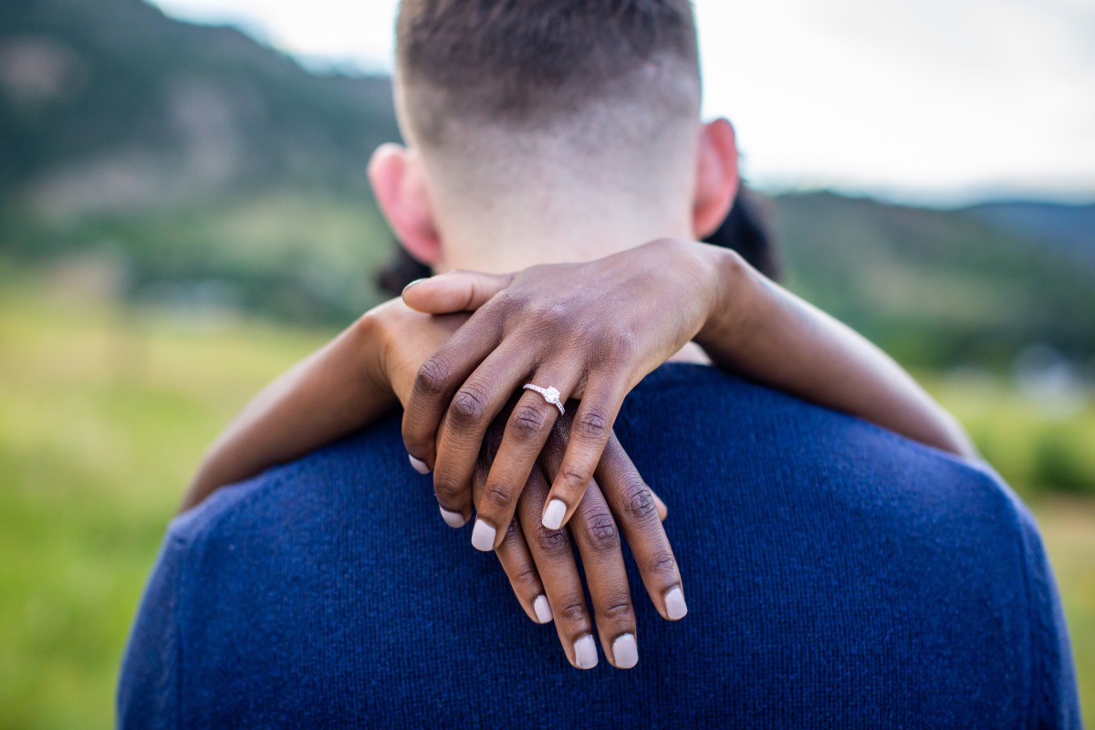 Engagement ring on hand embracing partner's neck