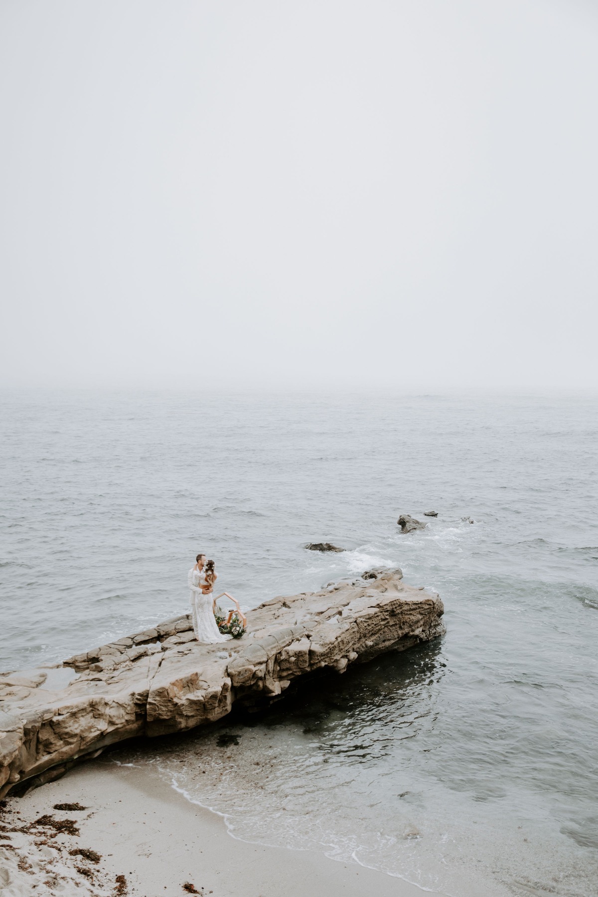 Bride and groom stand on rock at misty ocean wedding ceremony