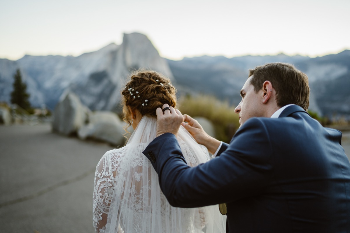 Groom helps bride with her veil near mountain peaks