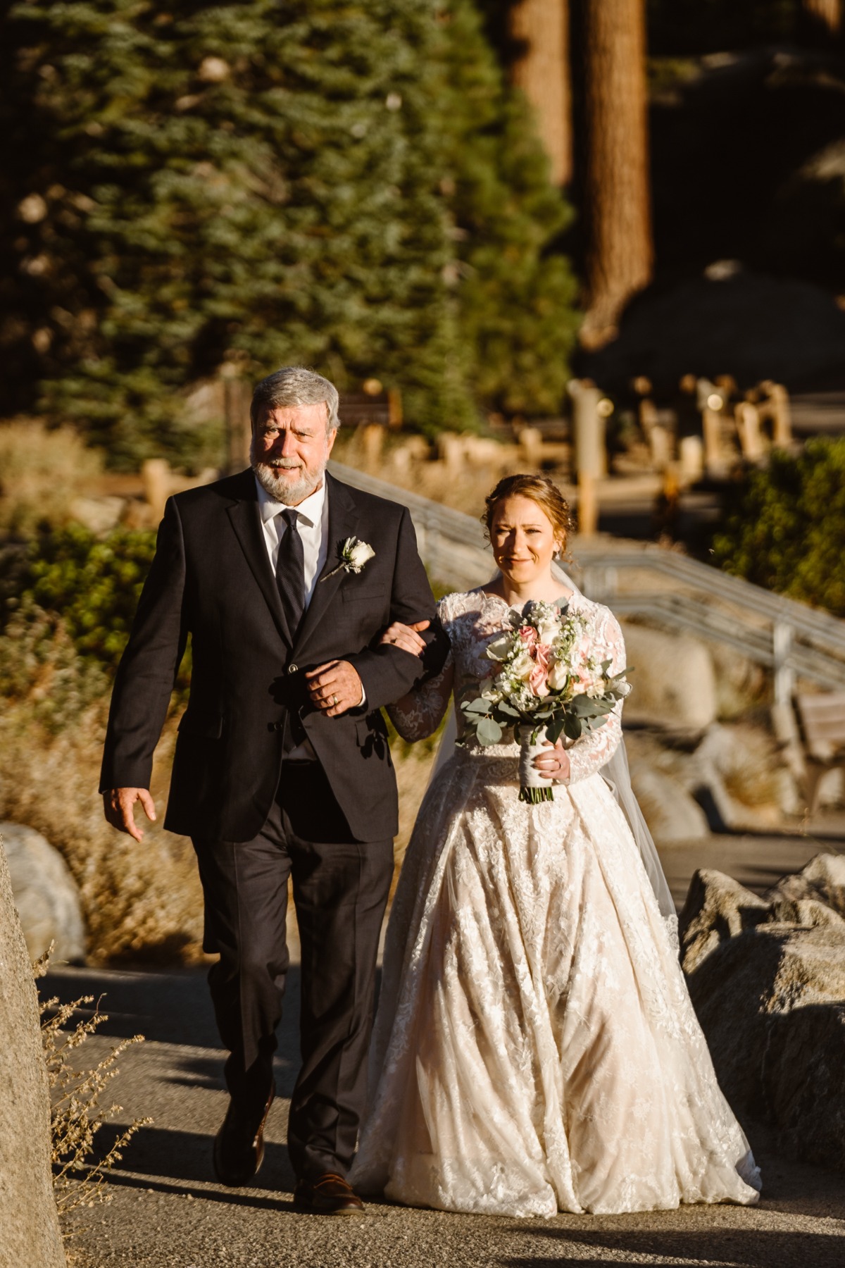 Father proudly escorts bride down sunlit outdoor path