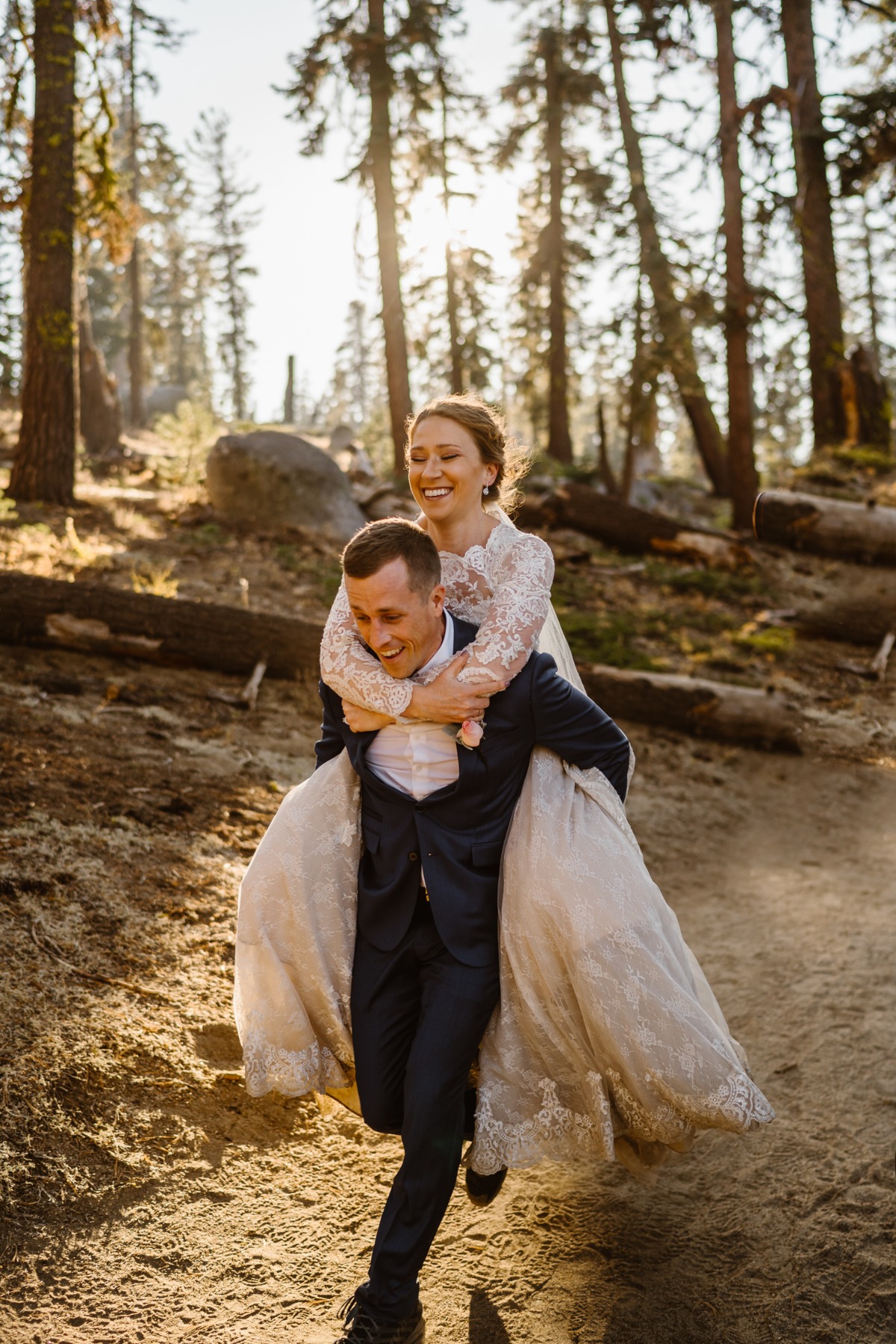 Happy groom gives laughing bride piggyback in woods