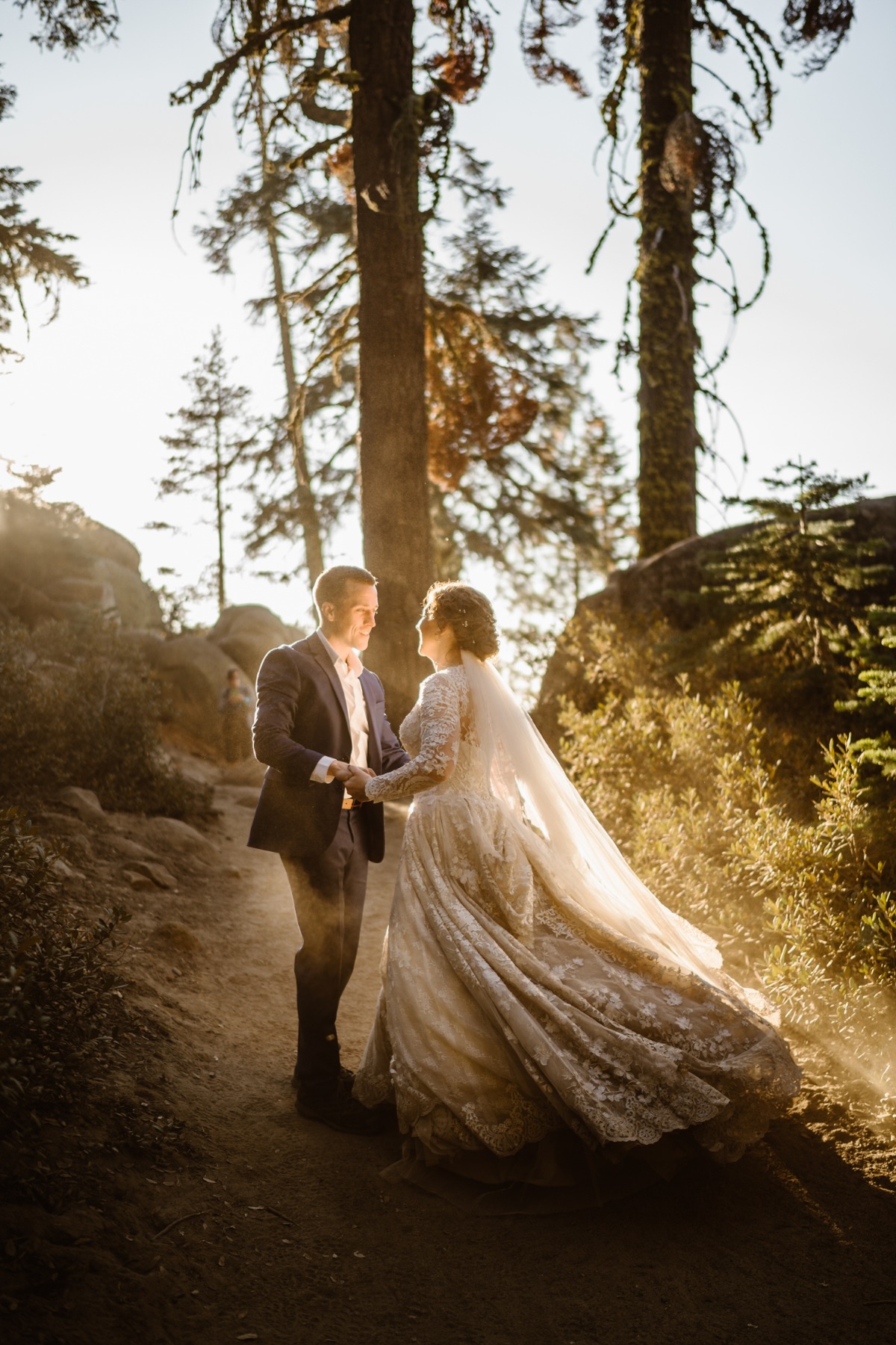 Bride and groom hold hands on a sunlit forest path