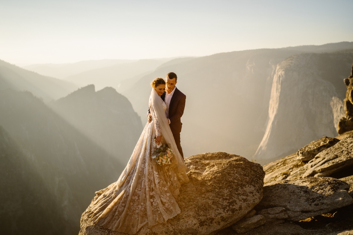 Newlyweds embrace on scenic mountain peak at sunrise