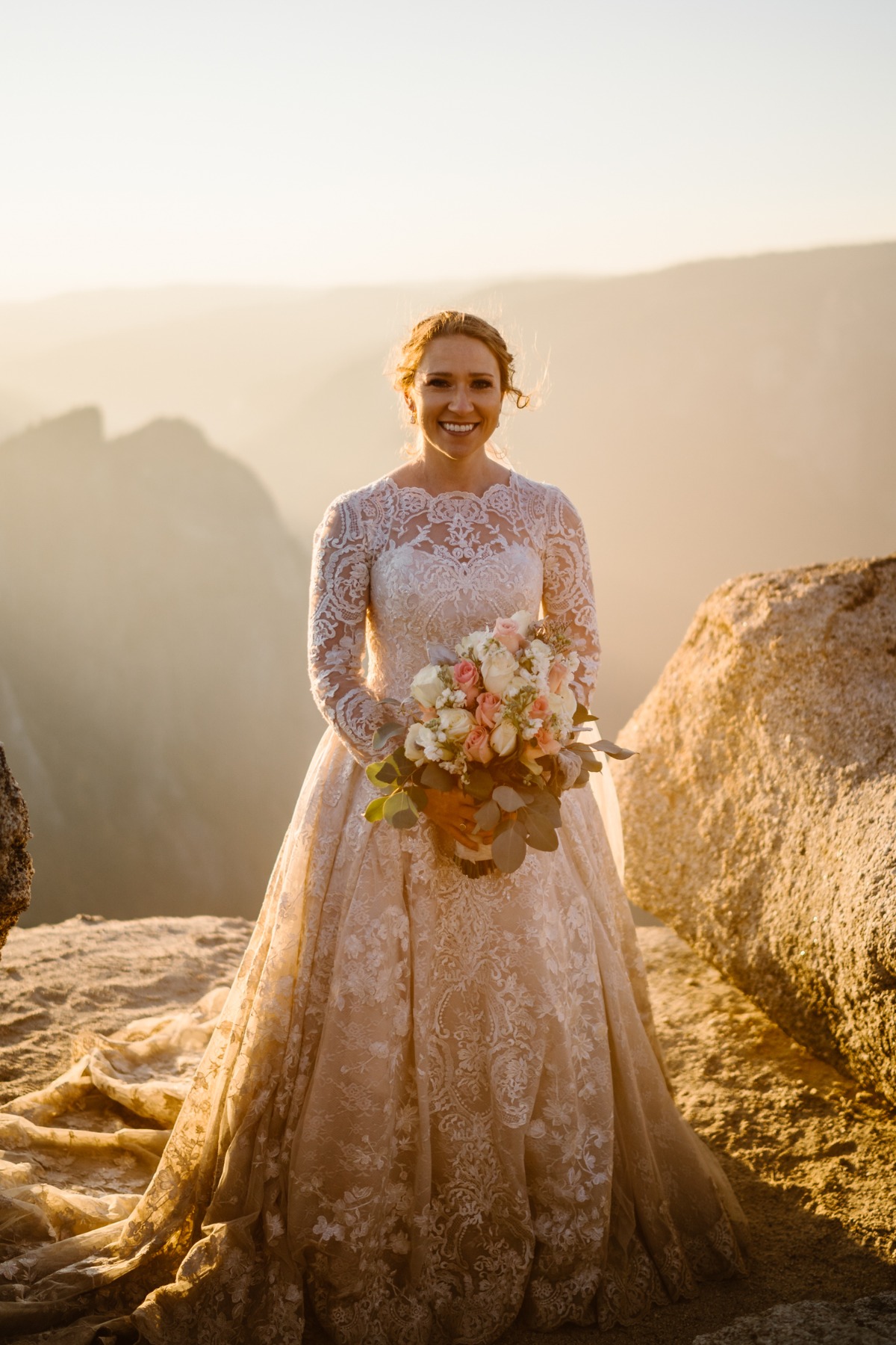 Radiant bride poses with bouquet on mountaintop overlook