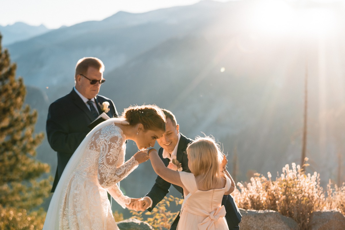 Bride kisses flower girls hand at mountain wedding ceremony
