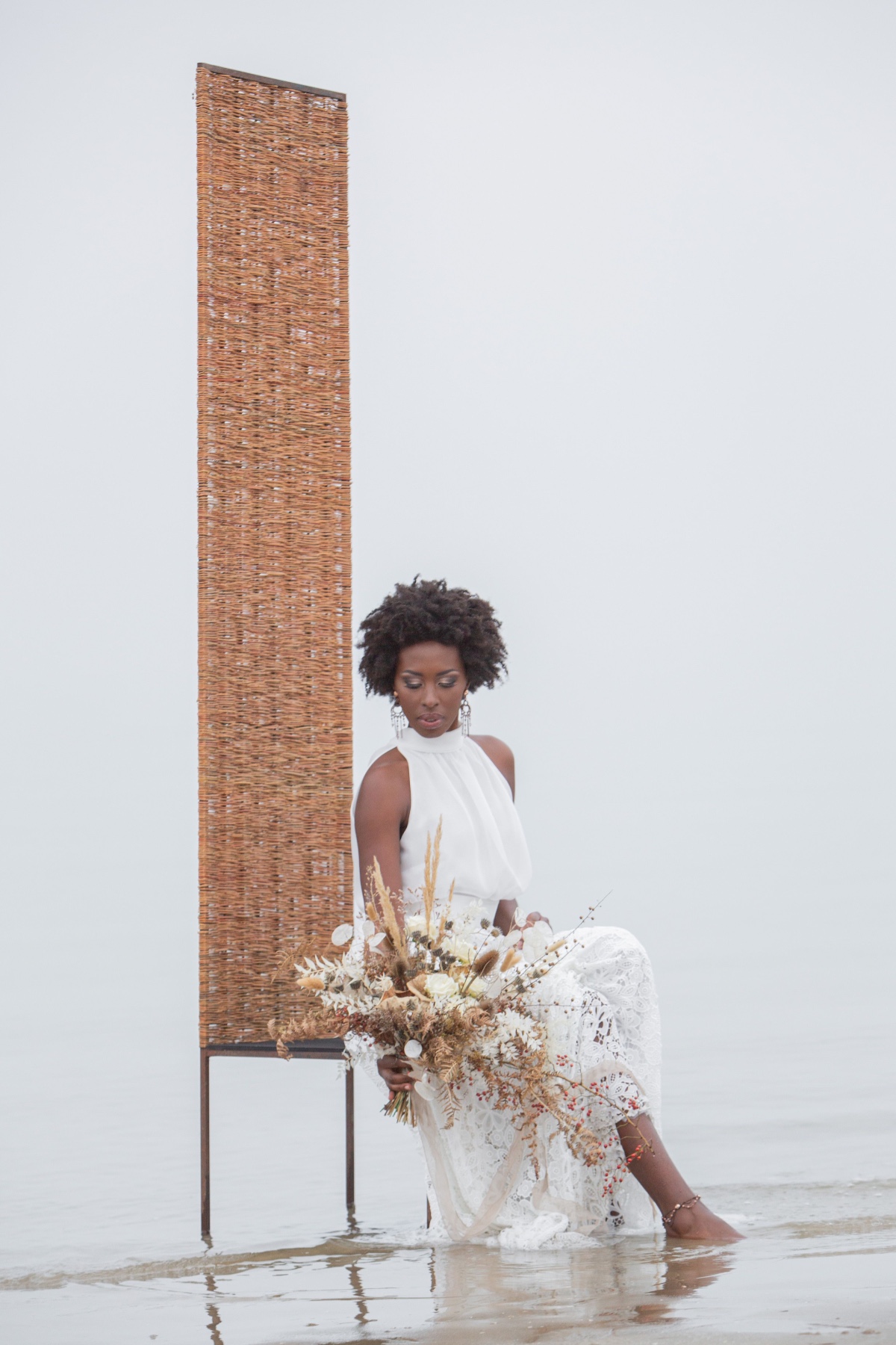 Bride in white dress with bouquet sitting on beach