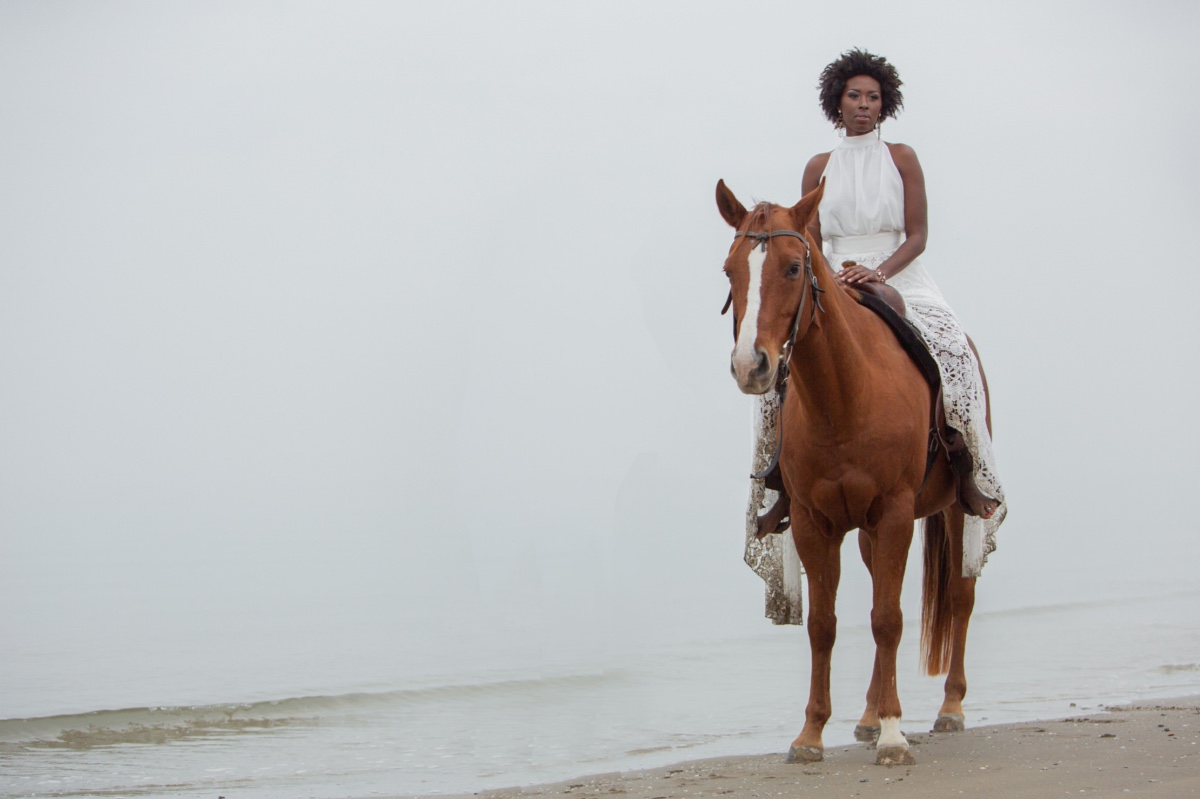 Woman in white dress riding a brown horse on the beach