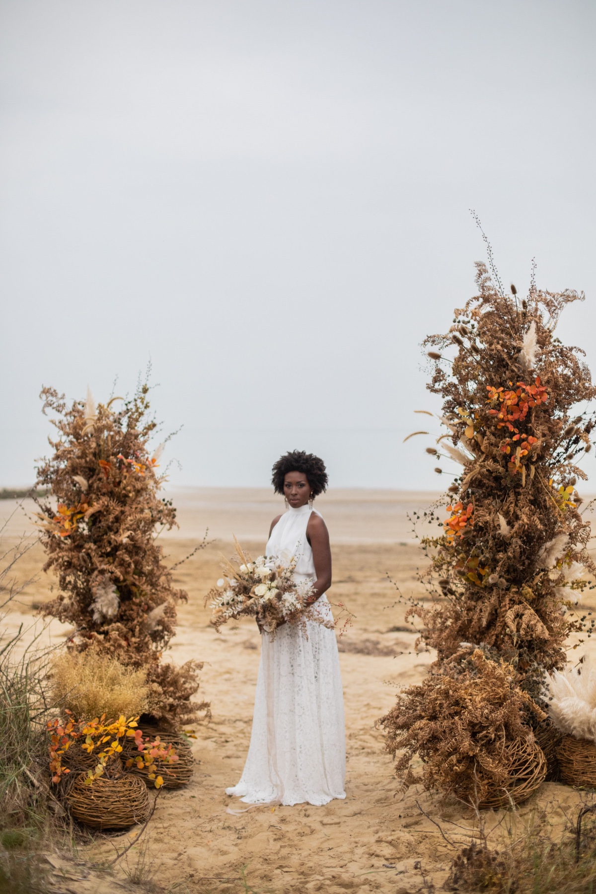 Bride in white dress, autumnal floral arch, beach wedding