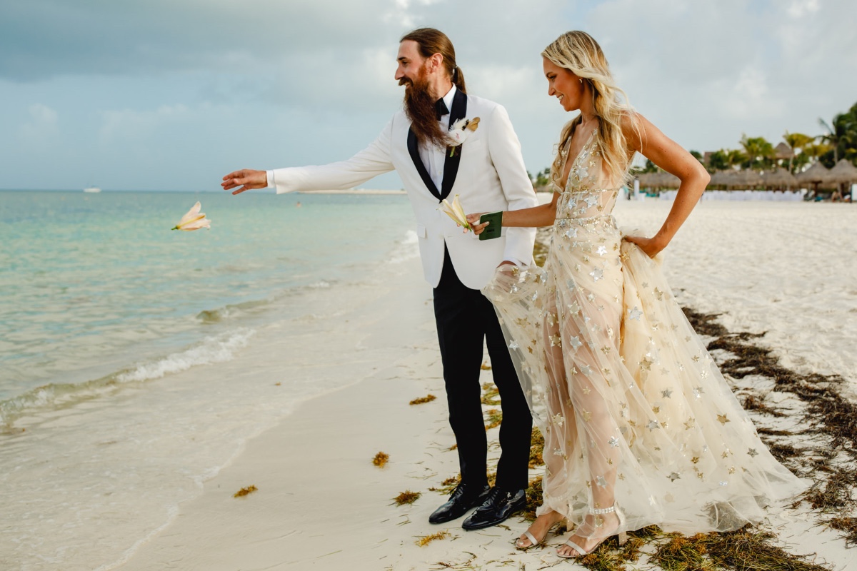 Happy wedding couple on beach throwing flower into water