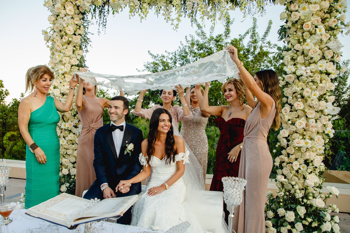 Bride and groom under wedding canopy with family support