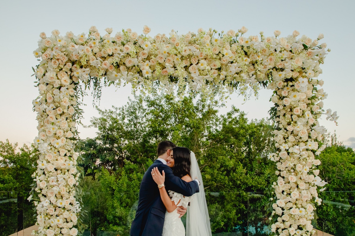 Bride and groom hug under floral archway at wedding