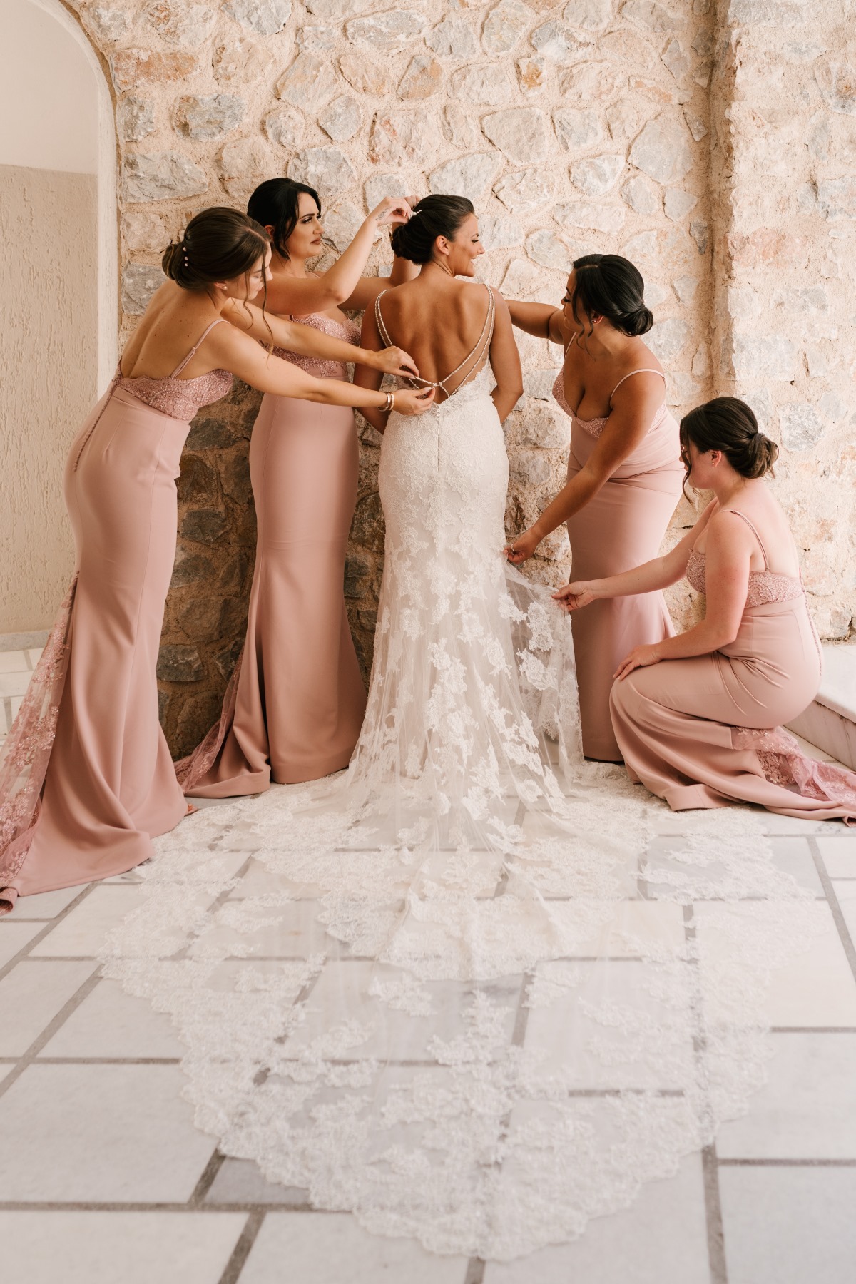 Bride gets help with dress from bridesmaids in pink gowns