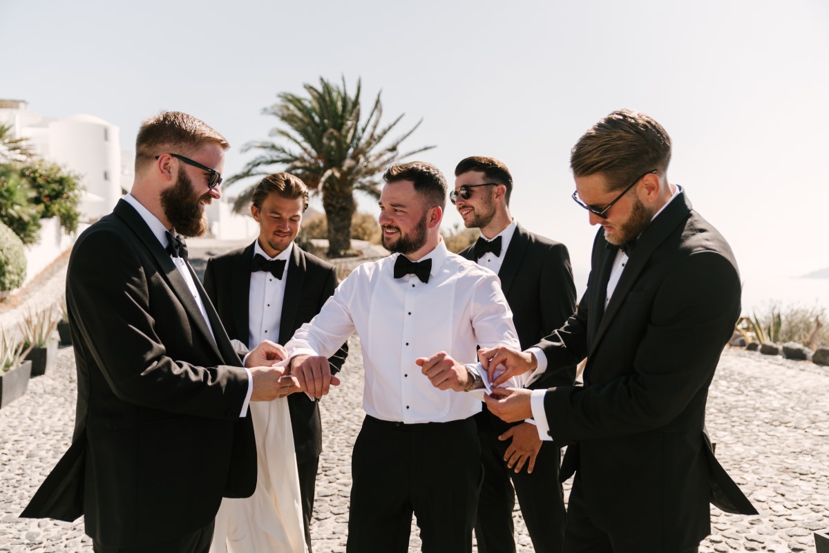 Groomsmen helping groom with cufflinks on wedding day