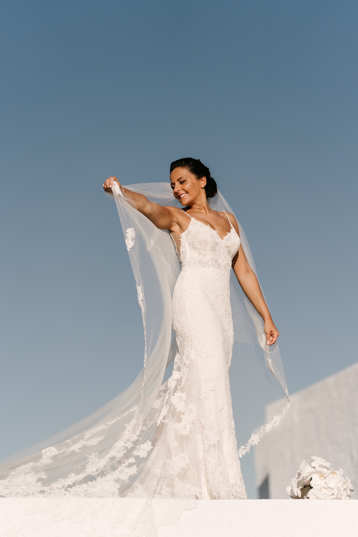 Happy bride in lace gown smiles under blue Santorini sky
