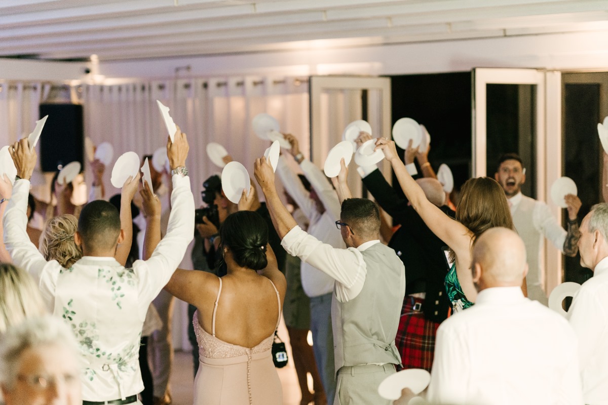 Wedding guests celebrate with plates in the air indoors