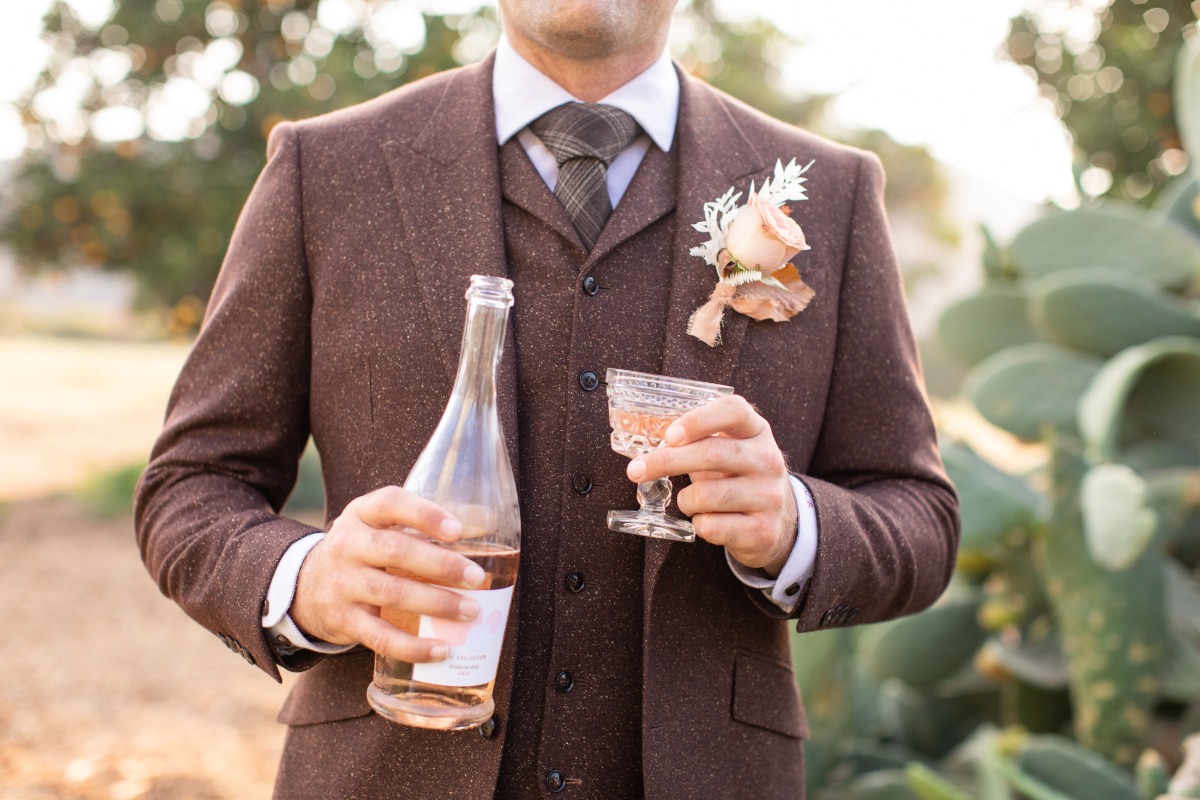 Groom in tweed suit holding rosé wine glass and bottle