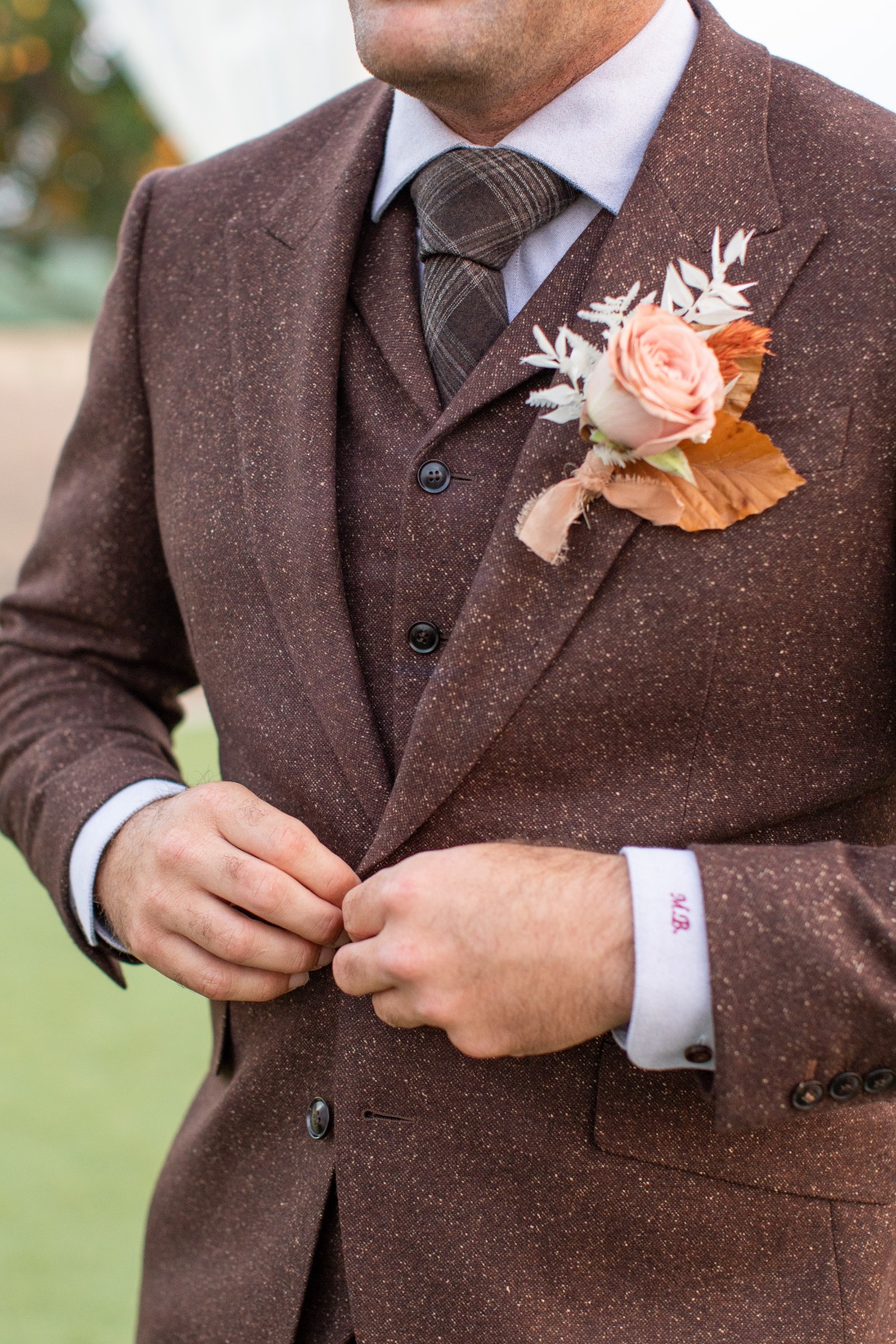 Groom in tweed suit with boutonniere buttoning coat