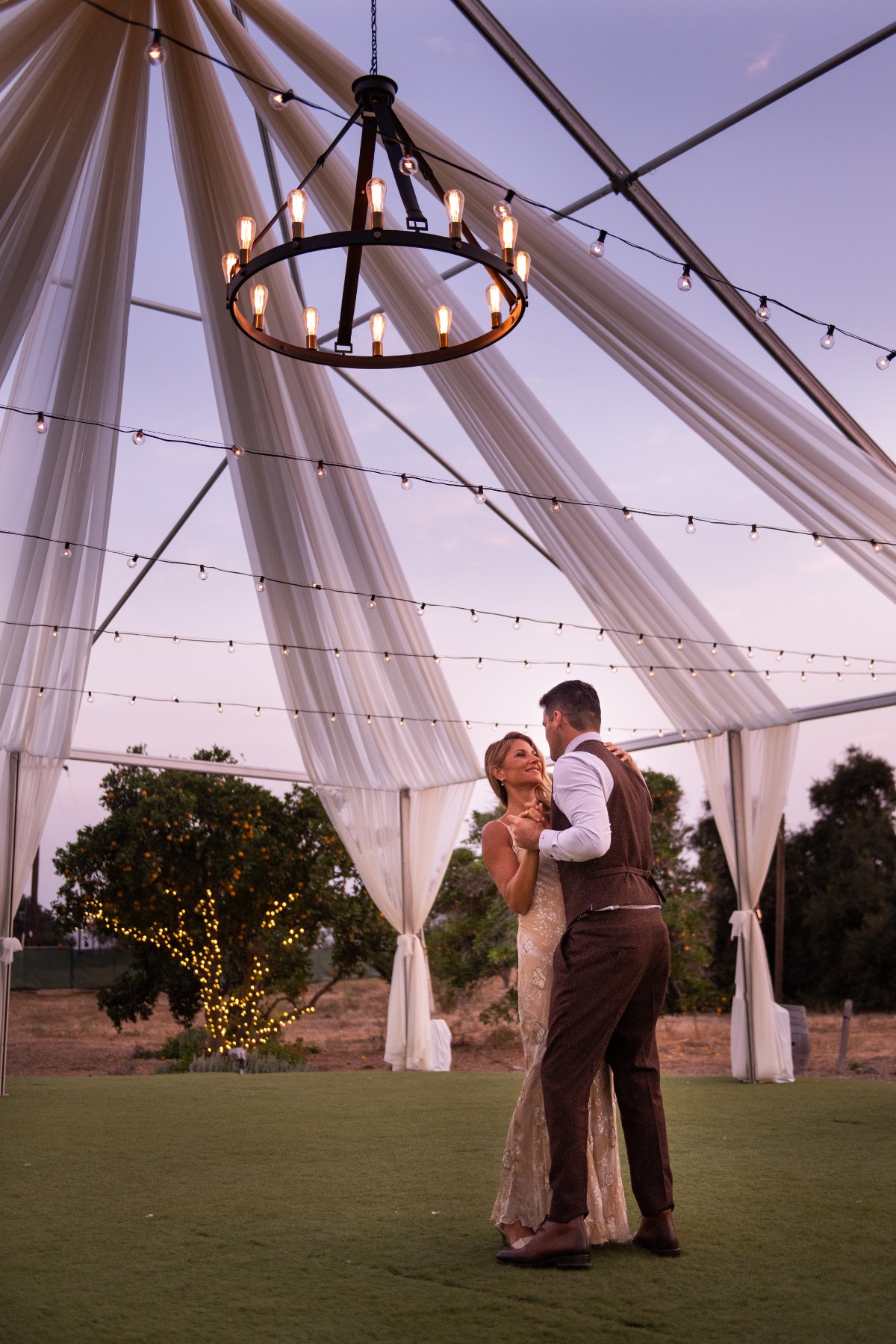 Newlyweds share their first dance under a tent at dusk