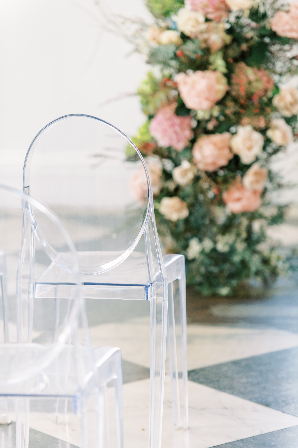 Ghost chairs and floral arrangements at wedding ceremony