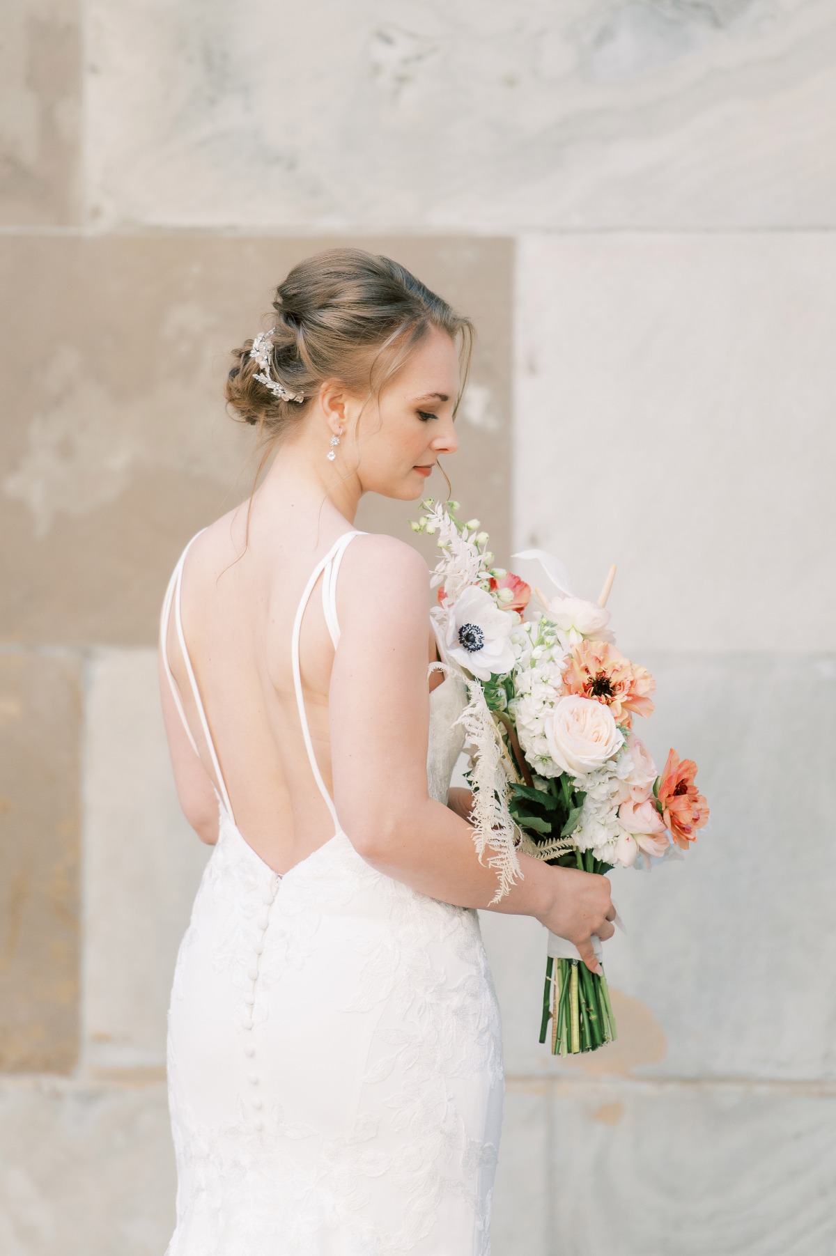 Bride in lace gown holds bouquet, elegant updo hairstyle