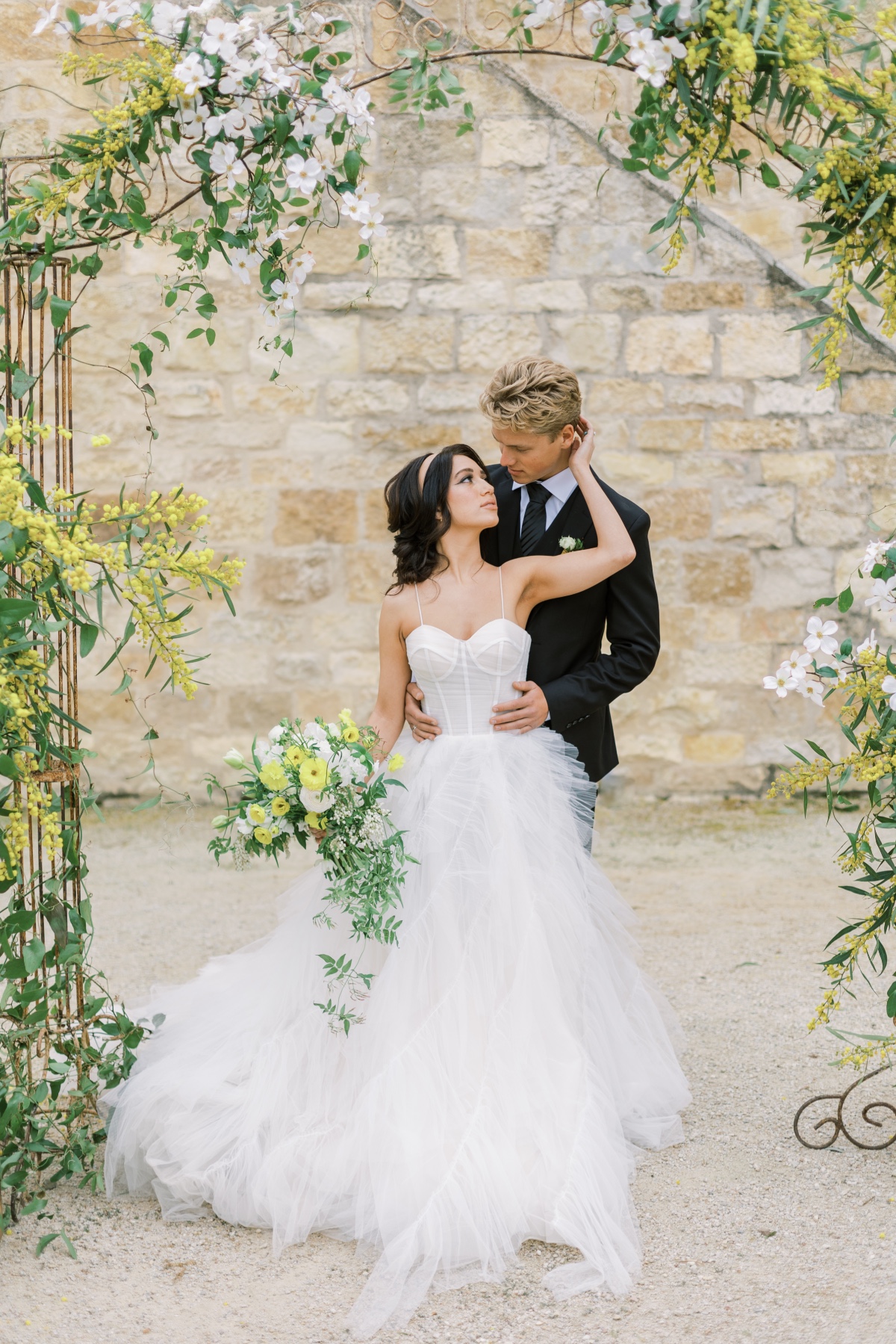 Romantic wedding couple embracing under floral arch
