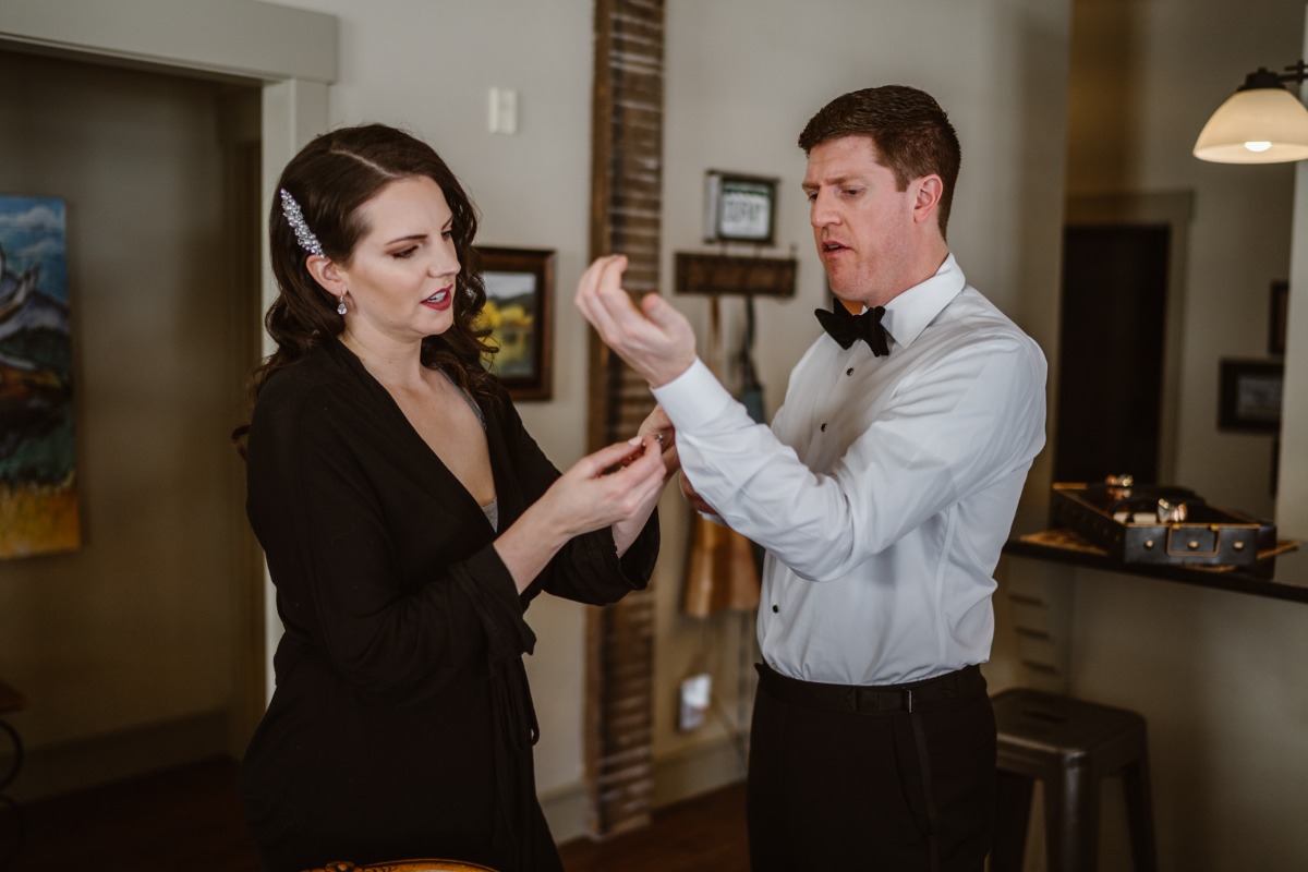 Bride helping groom with cufflink on wedding day preparation