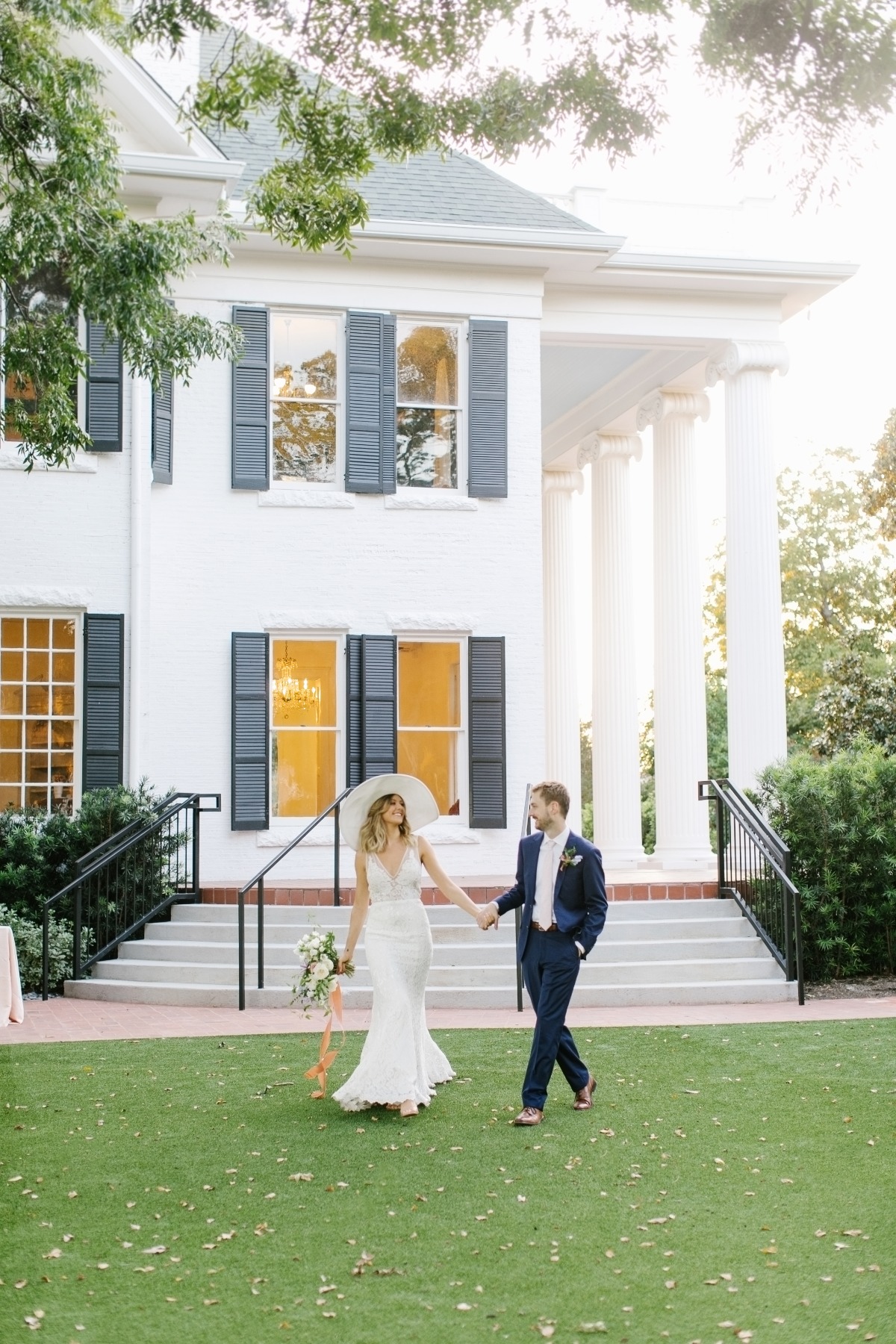Newlyweds holding hands at a wedding near a beautiful white house