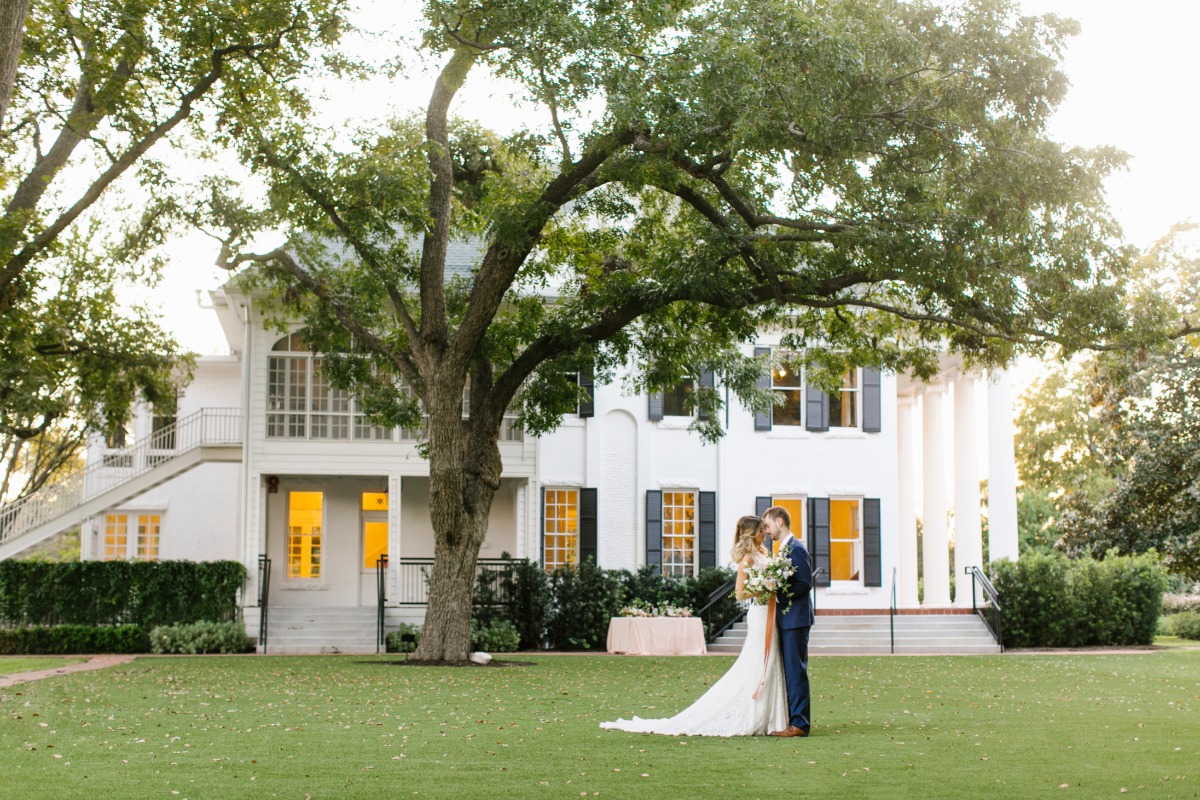Newlyweds embracing on the lawn in front of a grand estate during the wedding