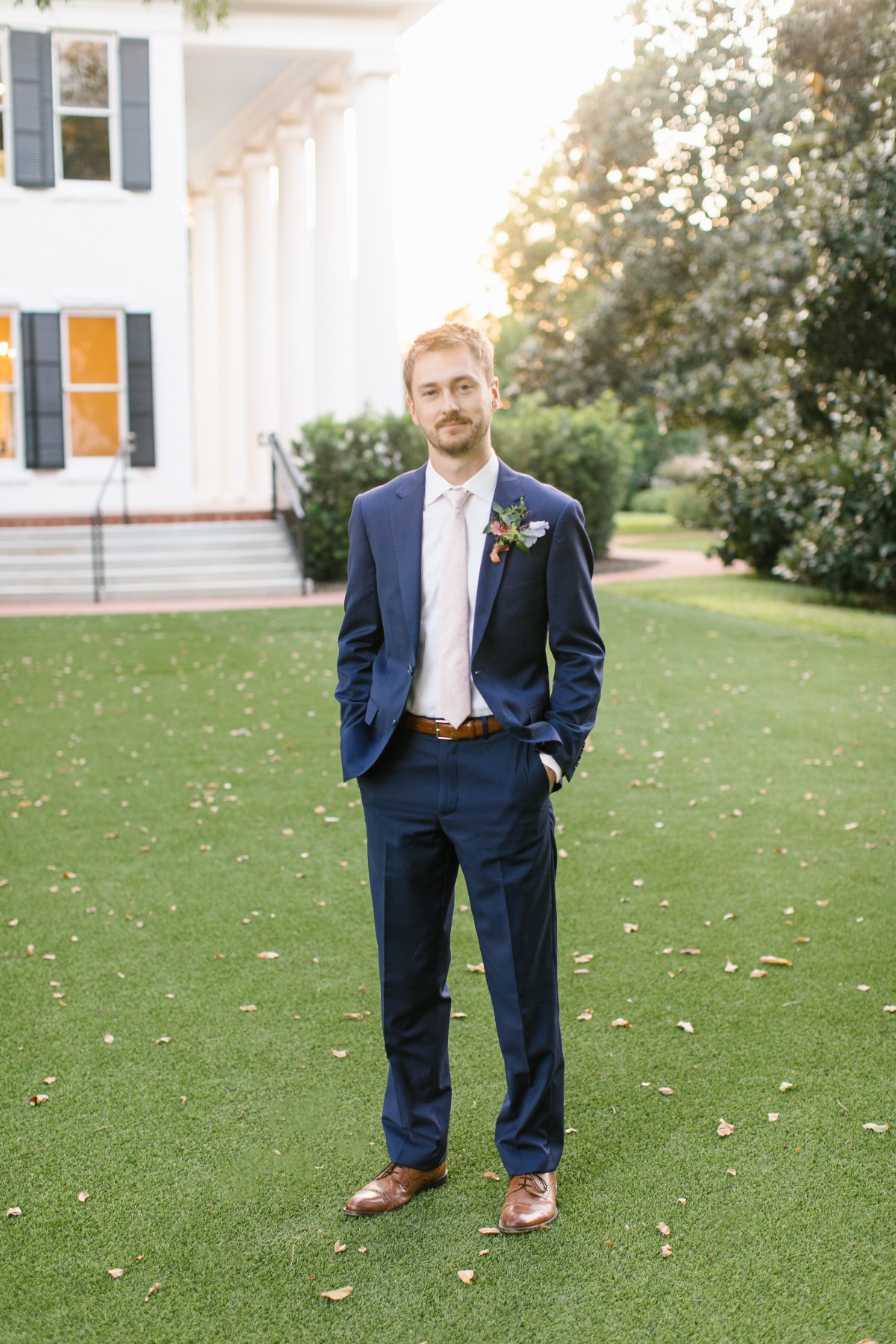 Stylish man in blue suit posing outside near a mansion