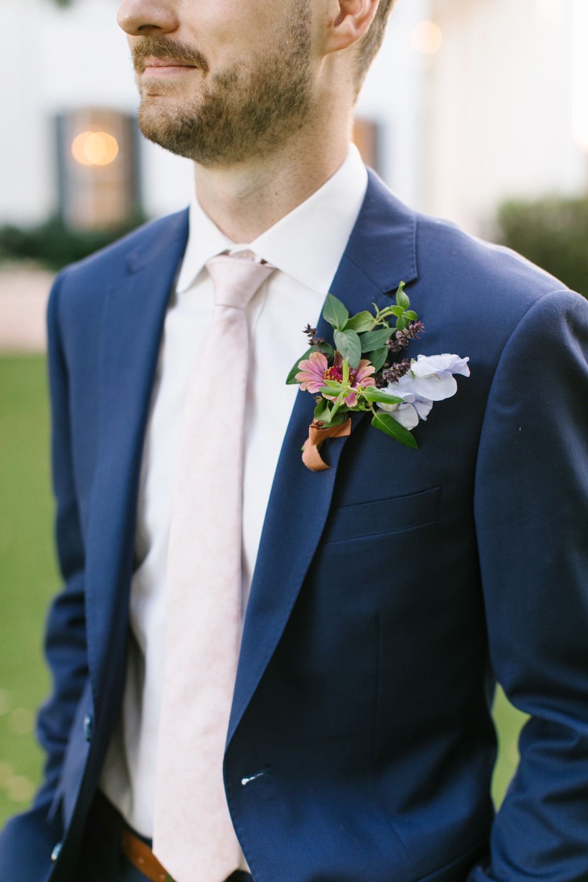 Groom in a navy blue suit with floral boutonniere smiles confidently at wedding