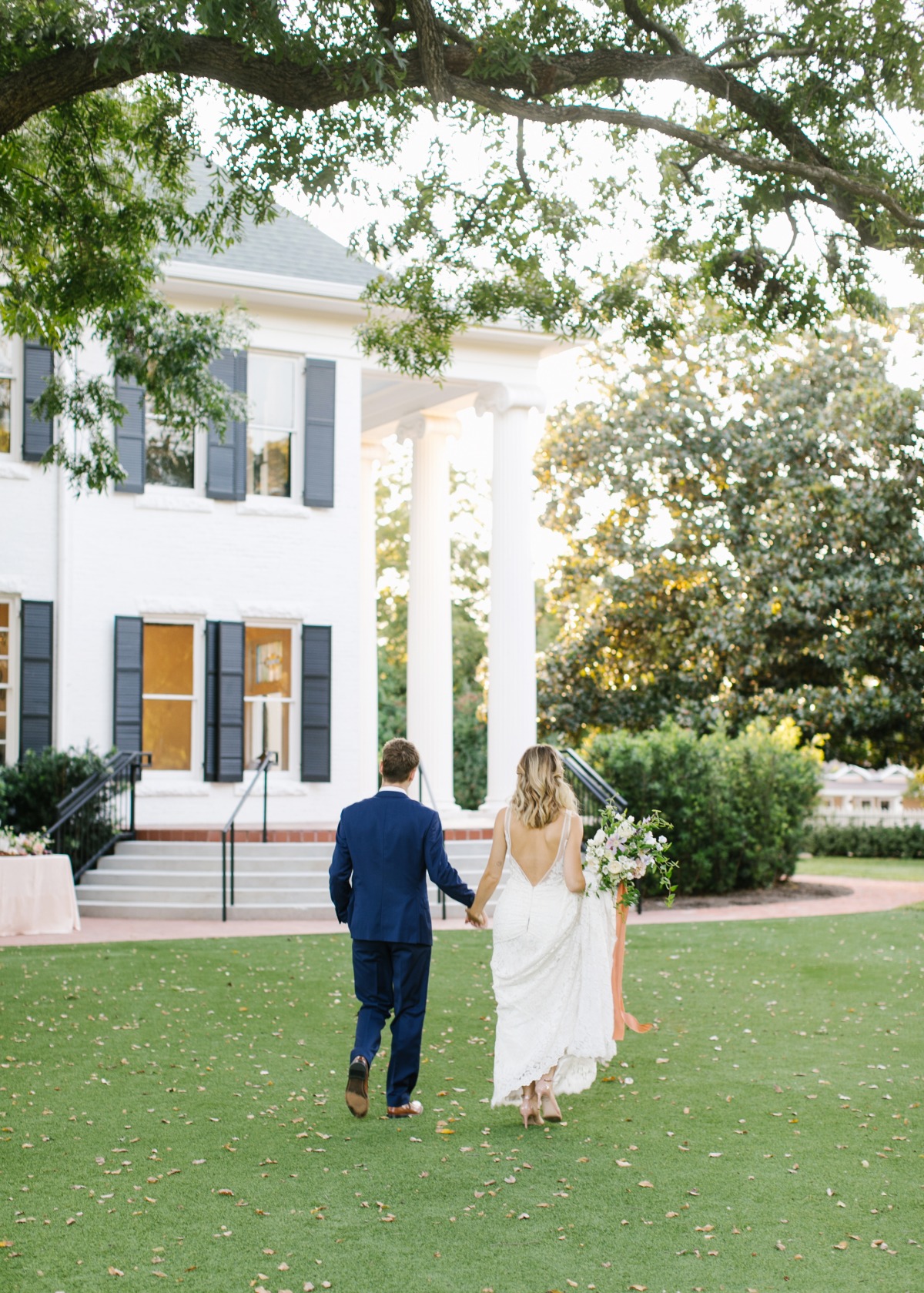 Newly married couple walks towards a grand white house at sunset
