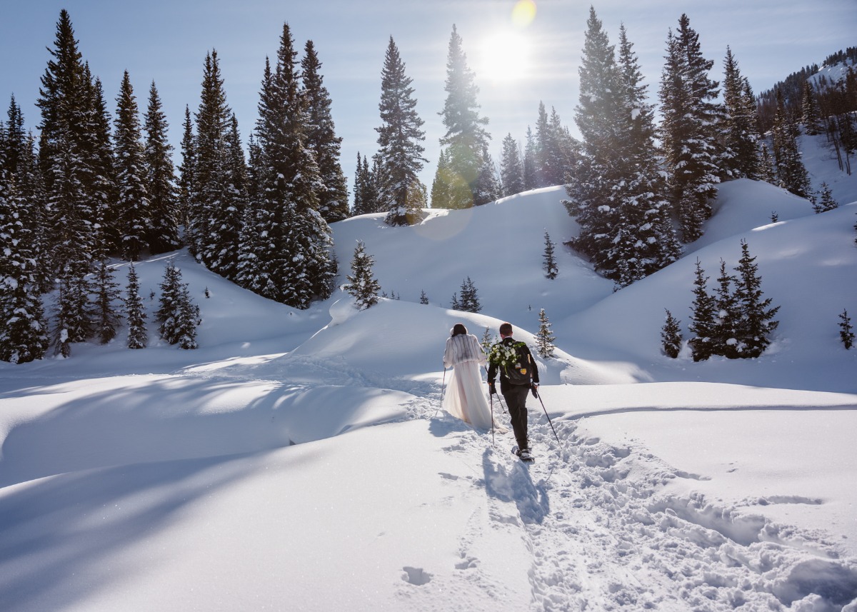 Newlyweds snowshoeing on a sunny, snowy mountain trail