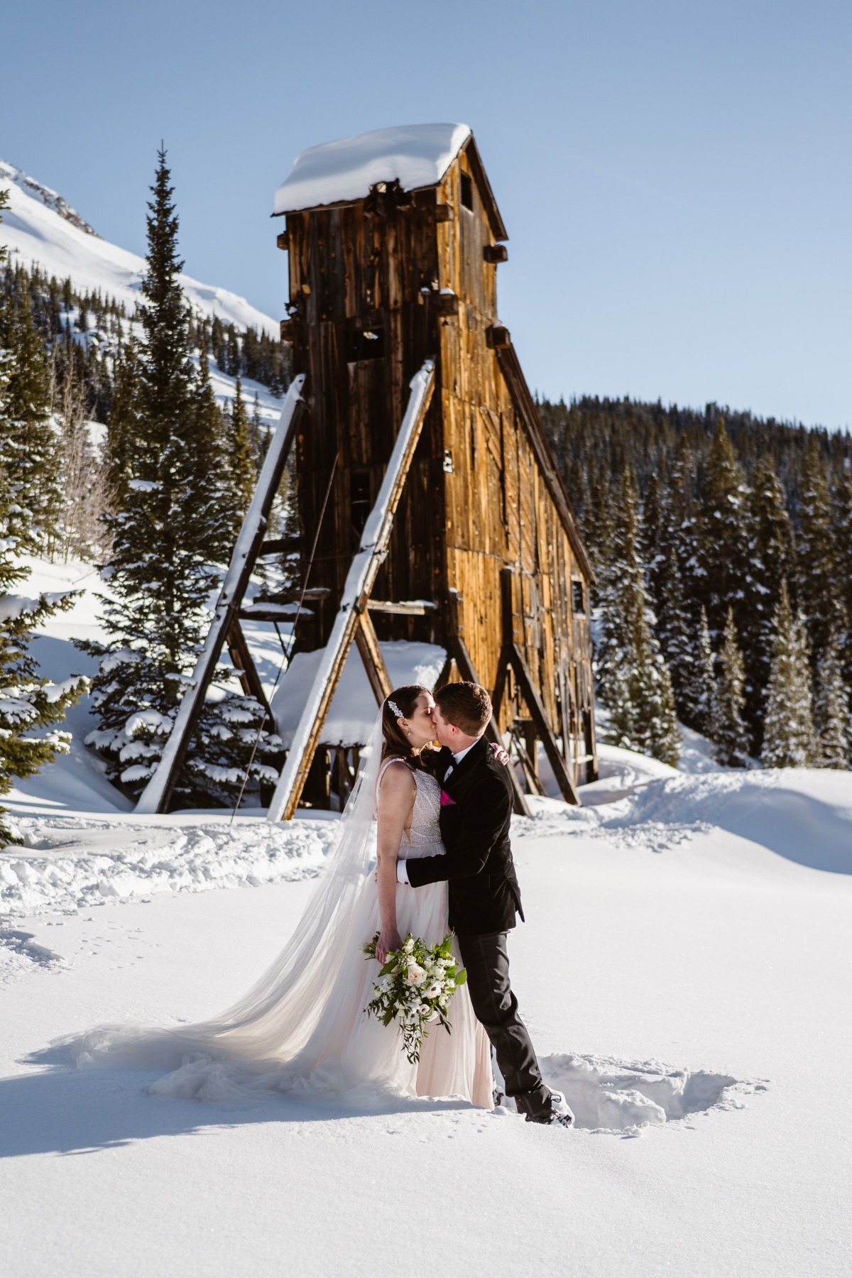 Newlyweds sharing a kiss in front of a rustic snow-covered cabin