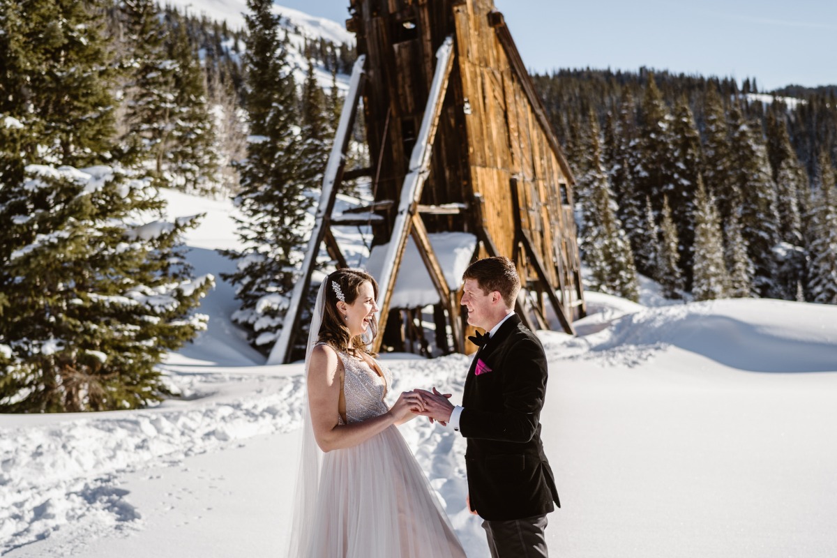 Happy couple sharing vows outdoors in snow with old wooden structure
